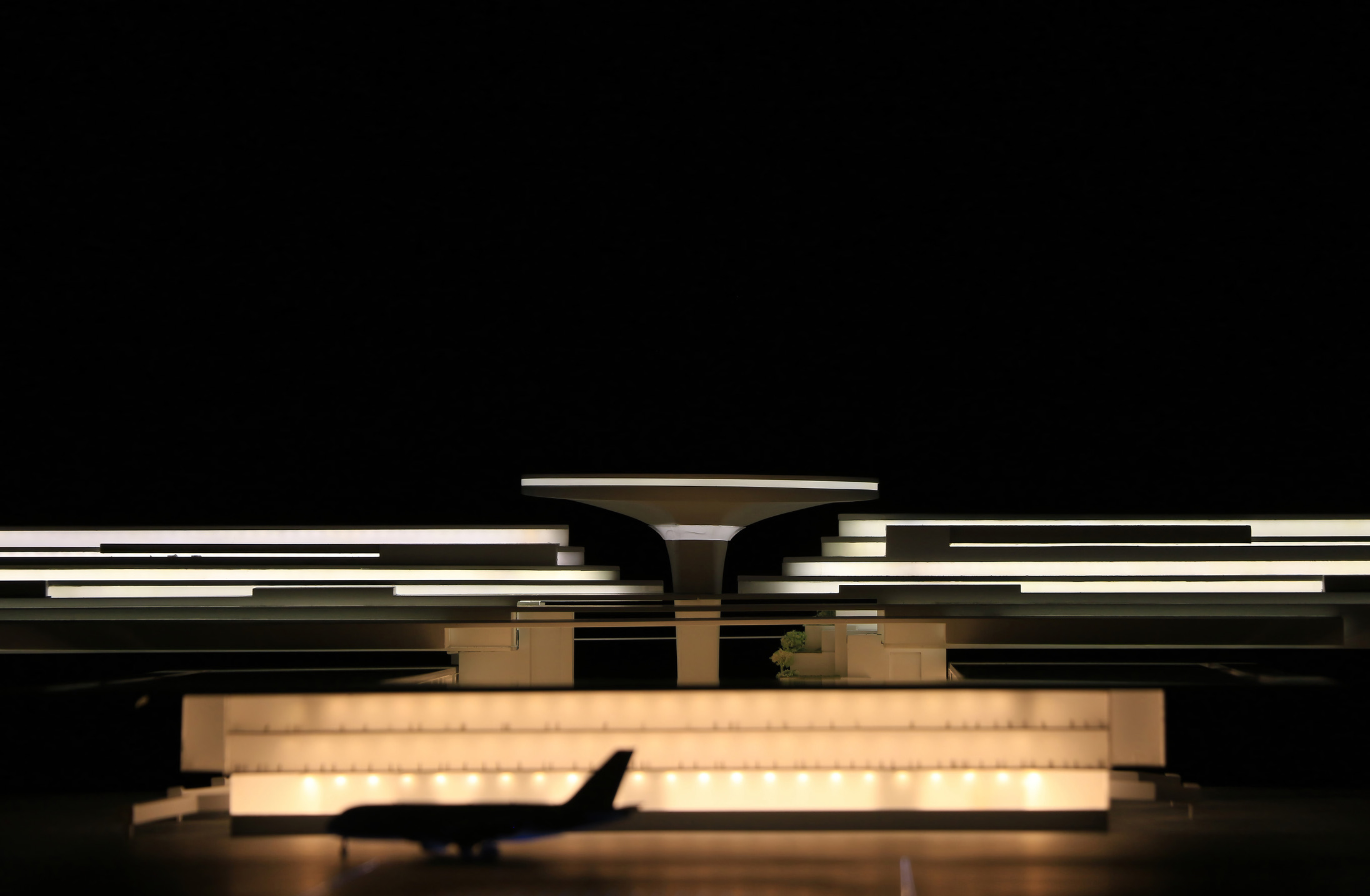 Physical model front elevation view showing the layered horizontal terminal structure with central sculptural tower element against a black background