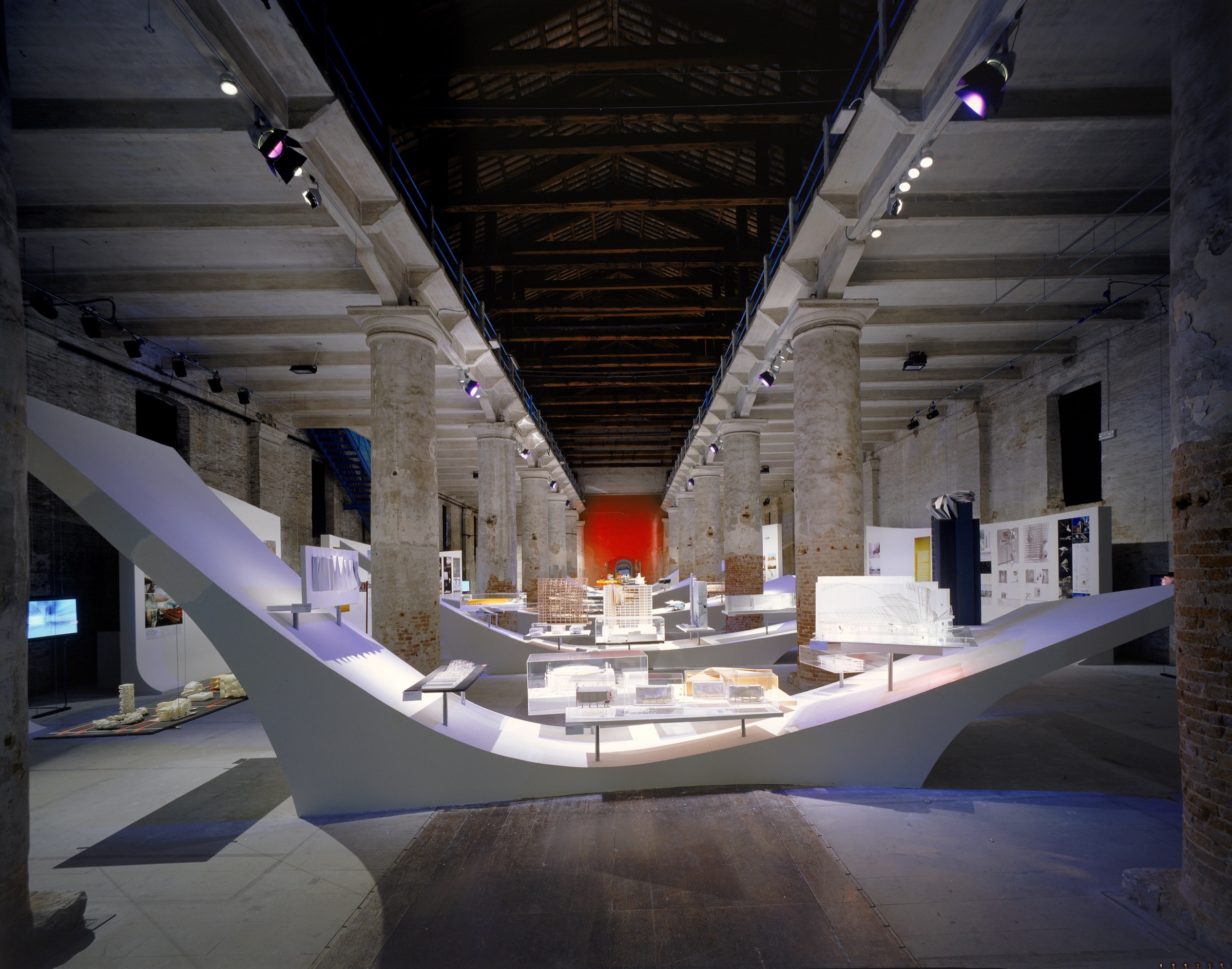 The Corderie dell'Arsenale transformed — sweeping white display surfaces with architectural models between the historic brick columns