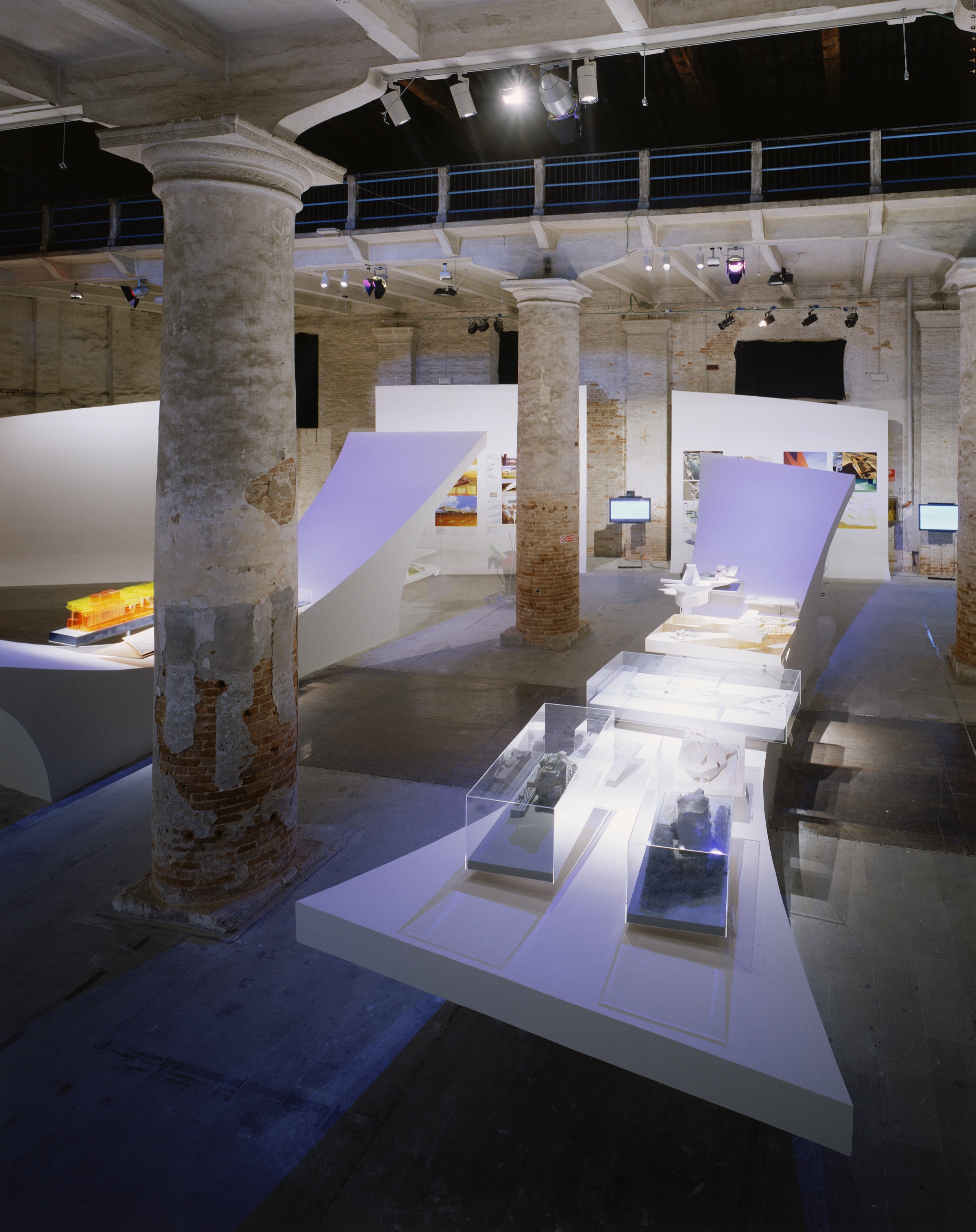 Deep perspective through the Arsenale — white sculptural display surfaces receding into the depth of the historic Corderie