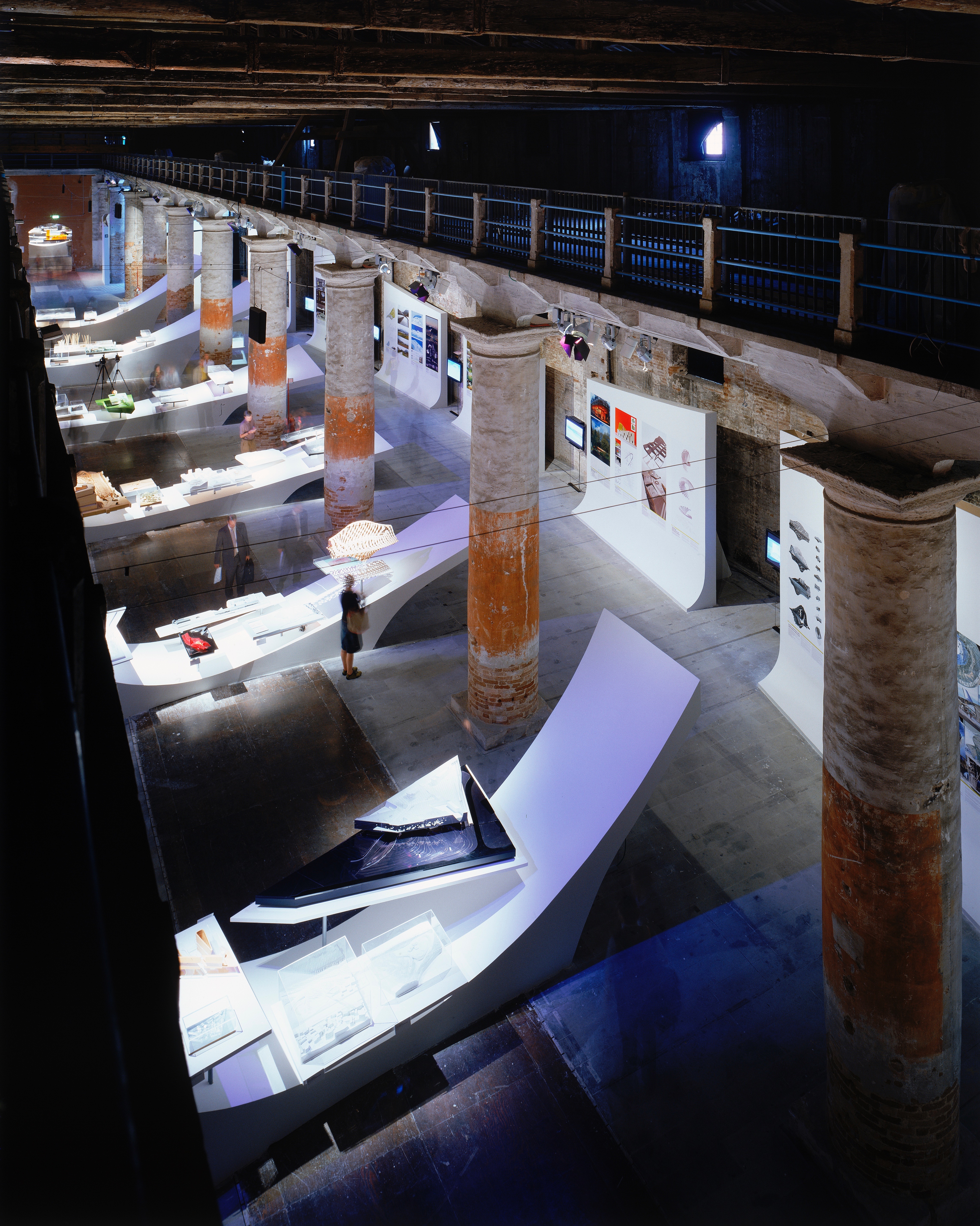 Asymptote's exhibition design for Metamorph at the 9th Venice Architecture Biennale — sweeping white display surfaces winding through the historic columns of the Corderie dell'Arsenale, showcasing works by over 150 architects
