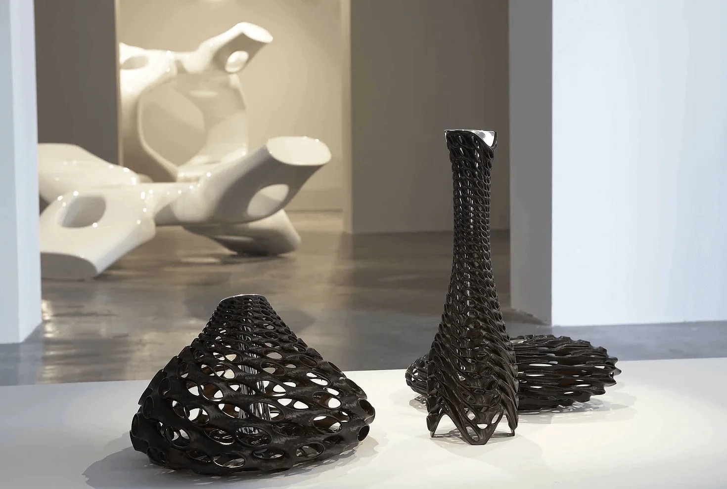 The three MGX vases installed at Atmospherics, Phillips de Pury — Ubu, Roi, and Fugu in black epoxy with chromed nylon inserts, a white M-scape sculpture visible beyond