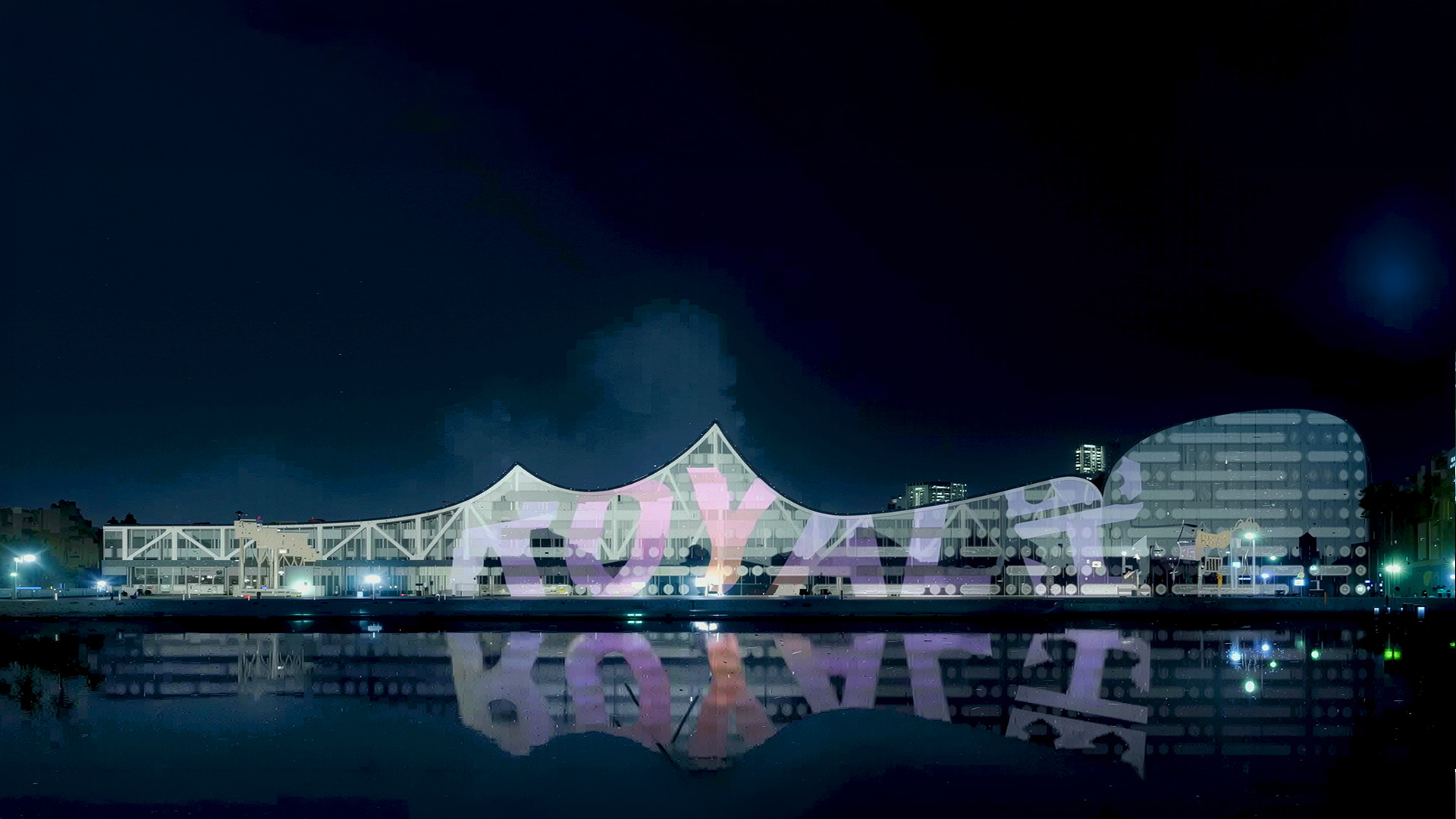 Night view of the Miami Port Terminal illuminated with Royal Caribbean branding projected across the sculptural facade, reflected in the harbor waters
