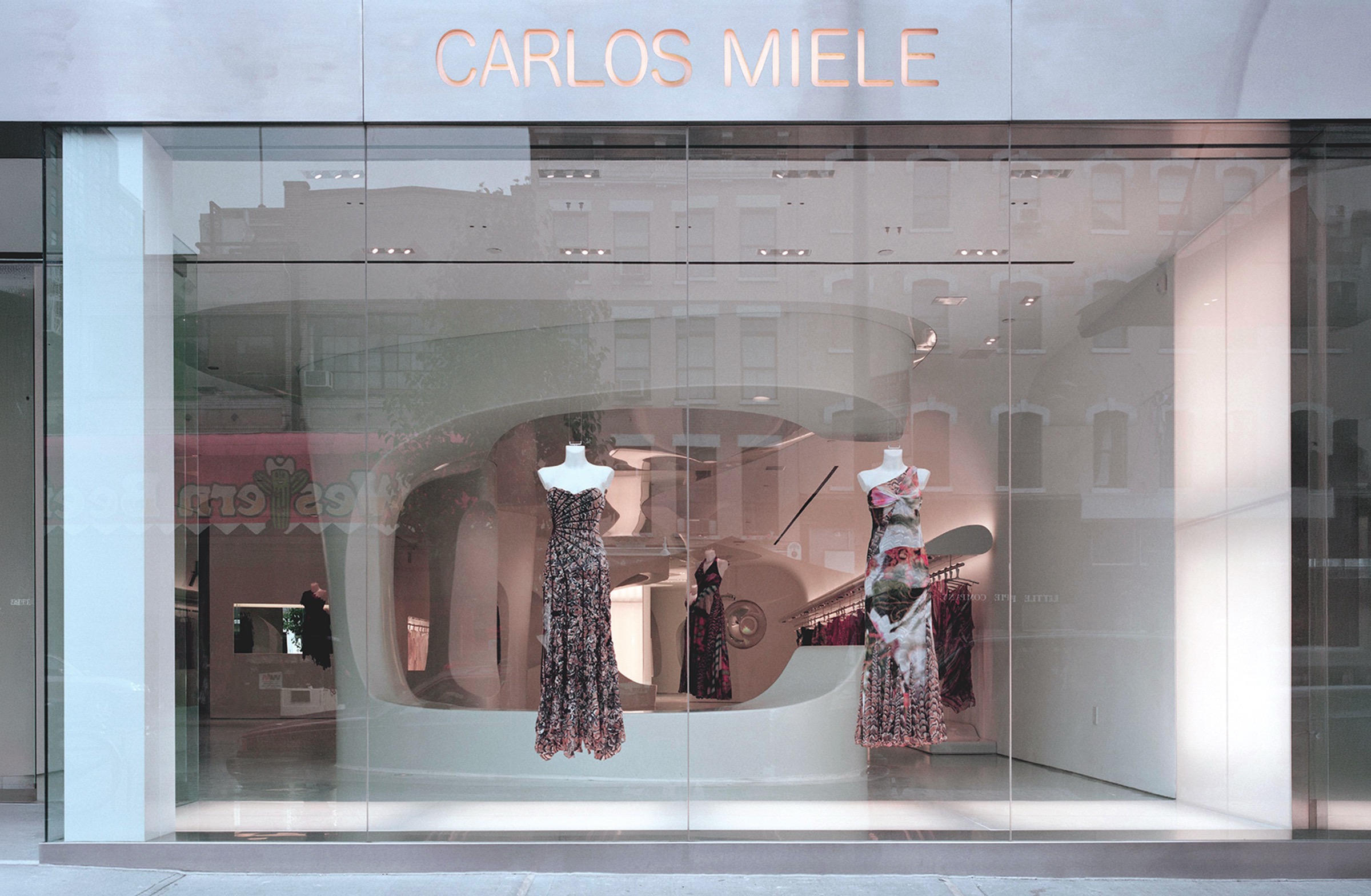 Exterior storefront of the Carlos Miele Flagship Store in the Meatpacking District with full-height glass facade, CARLOS MIELE signage, and mannequins displayed within the curvilinear white interior