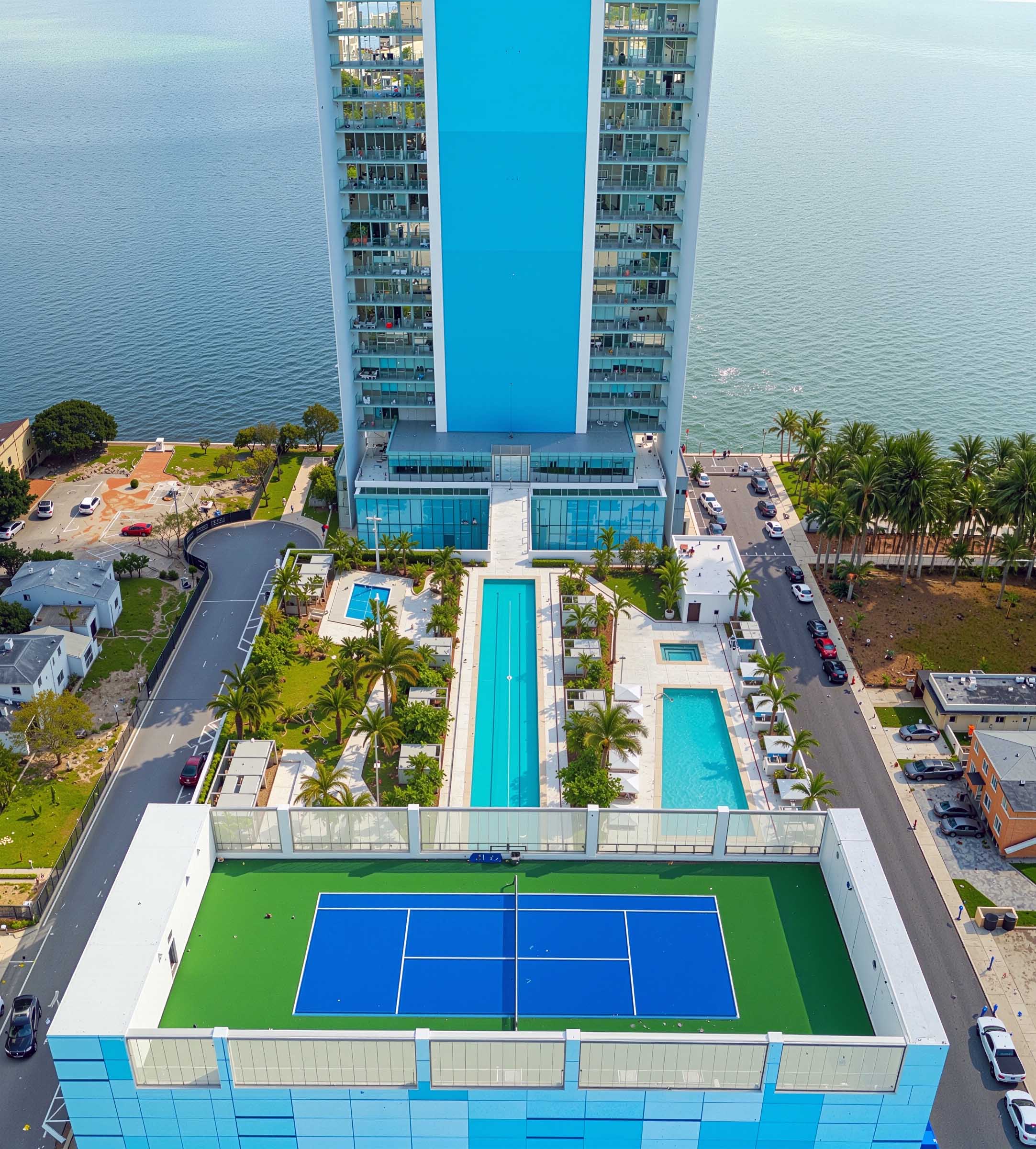 Aerial drone view of the Missoni Baia amenity deck featuring lap pools, landscaped gardens, tennis court, and the bay beyond