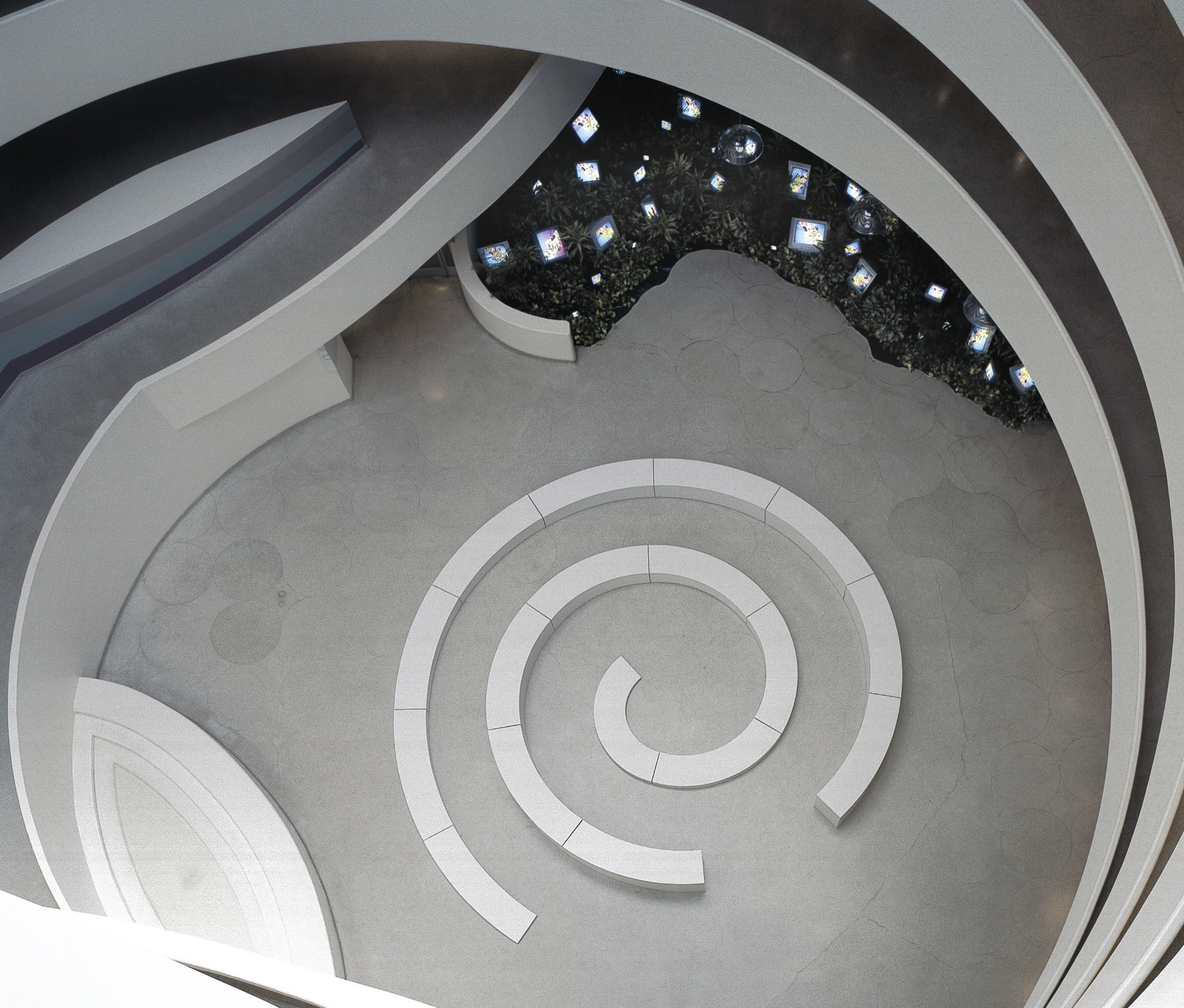 Overhead view looking down into the Guggenheim rotunda floor — spiral seating bench on the ground level, video screens glowing on the upper ramps