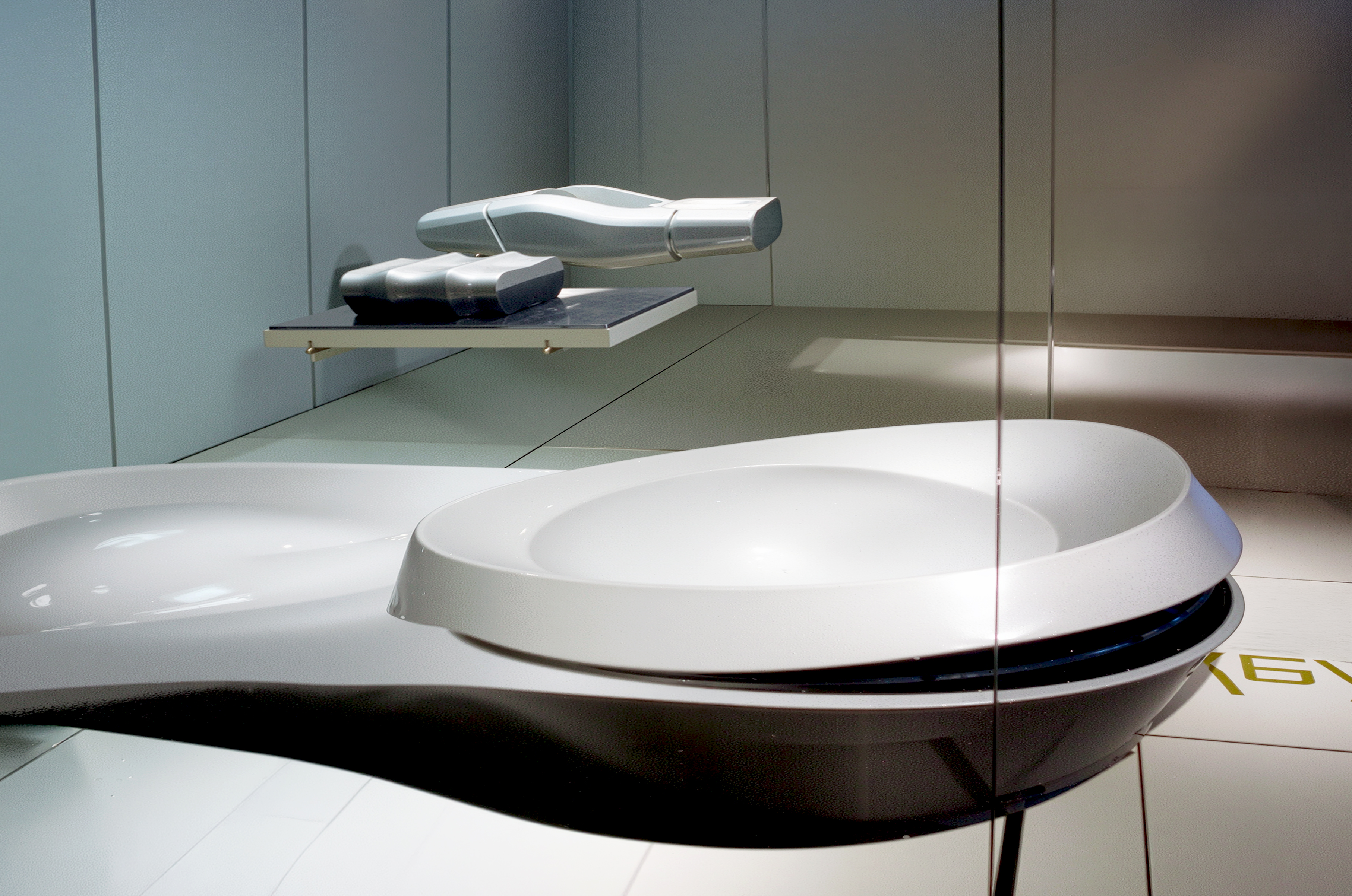 Close-up of Asymptote's models — a biomorphic white form and metallic sculpture on suspended glass shelves