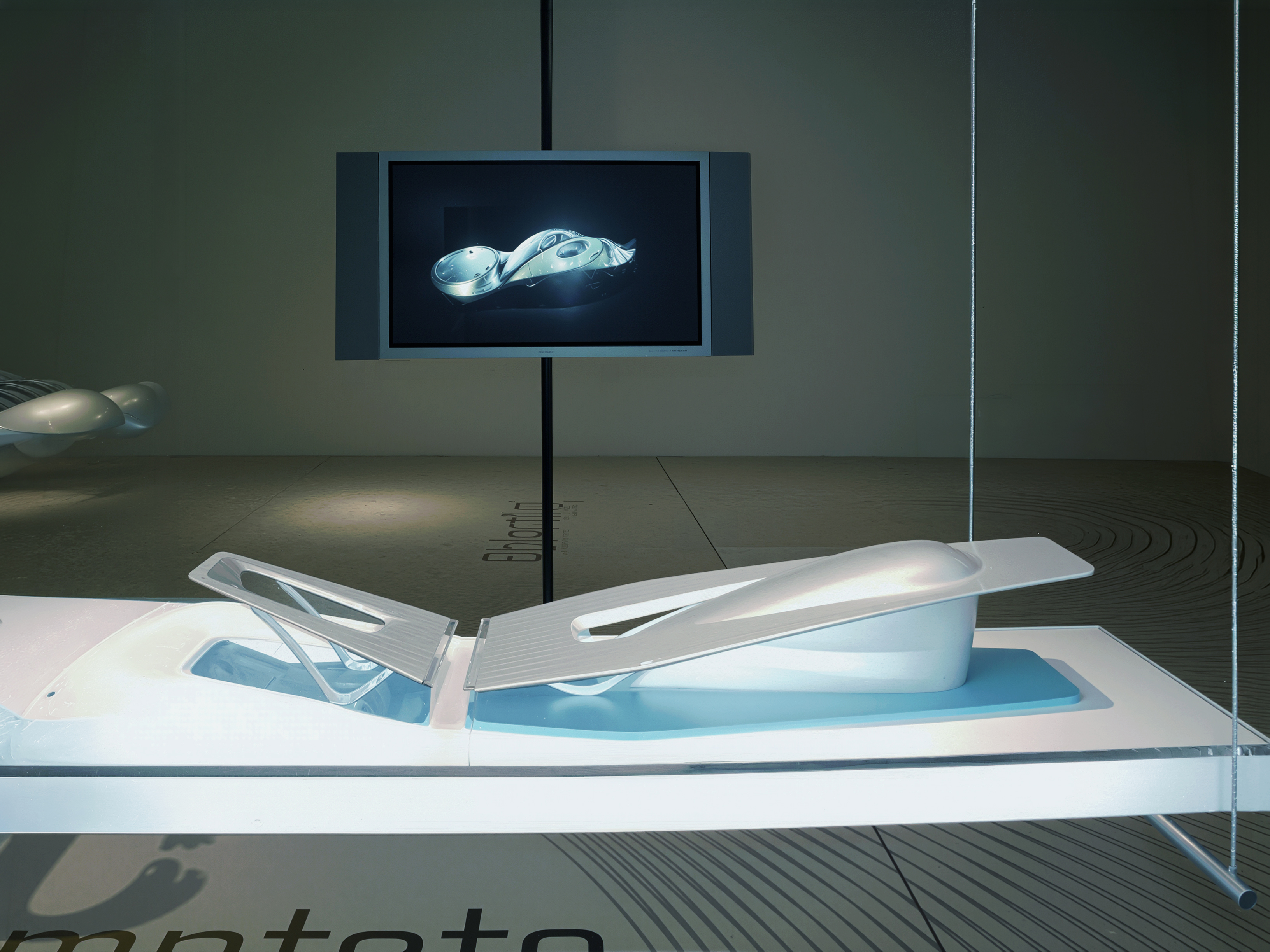 Asymptote's architectural model on an illuminated platform with a screen displaying a digital rendering behind it