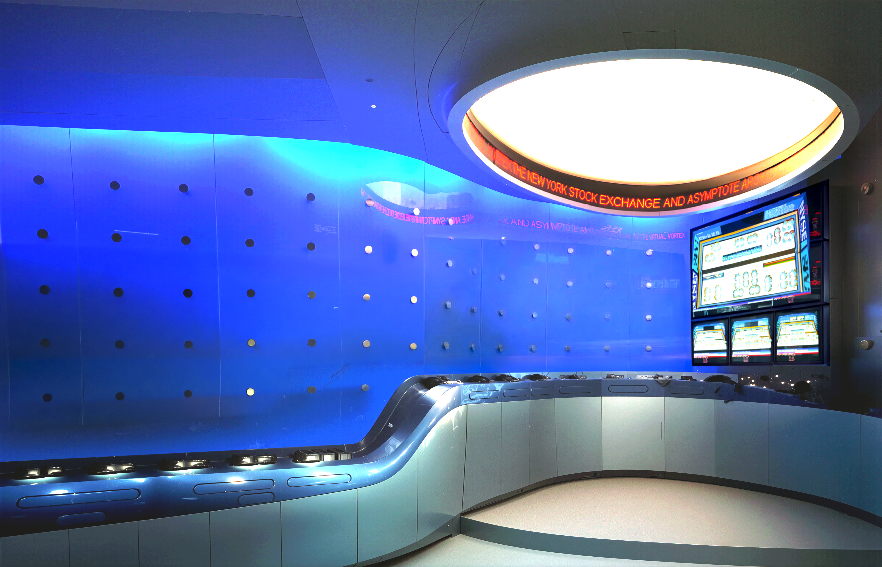 Illuminated blue glass wall with perforated pattern, curved stainless steel desk, and oval ceiling light with scrolling NYSE ticker