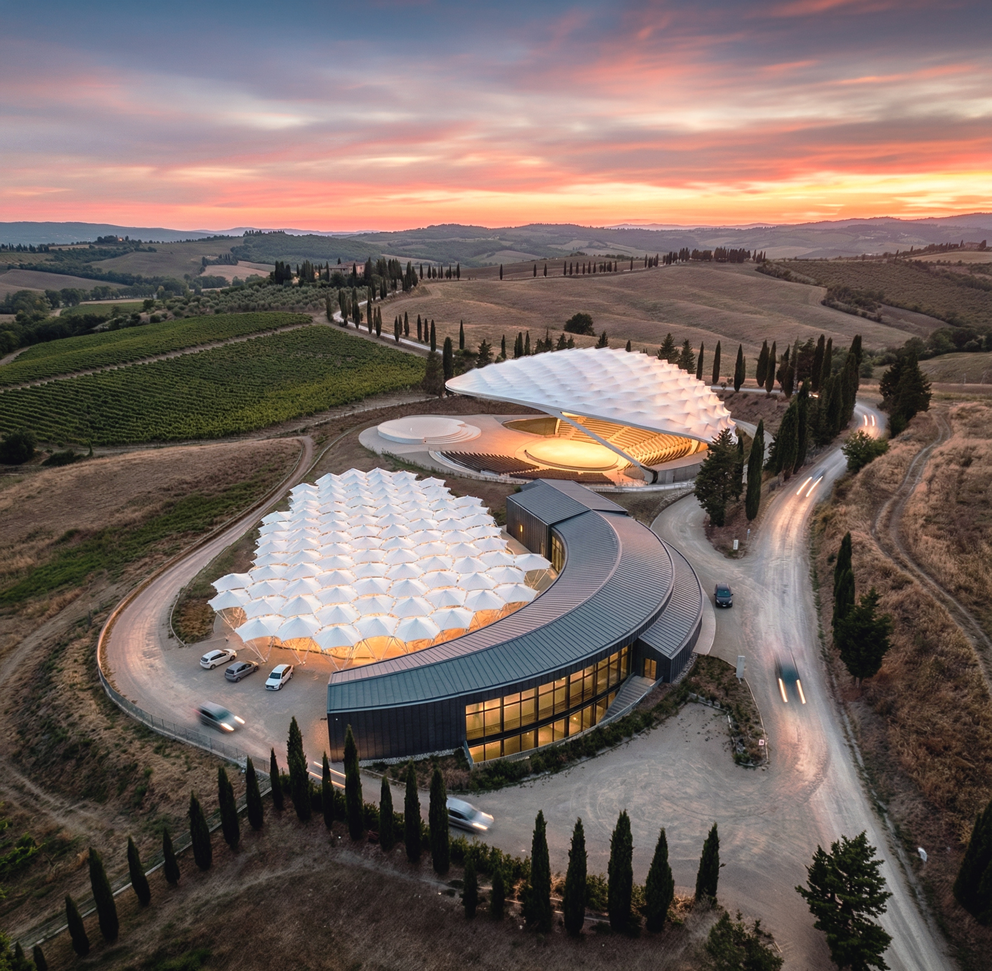 Aerial sunset view of the Park of Angels complex with its organic white canopy structures nestled among Tuscan cypress trees and rolling hills