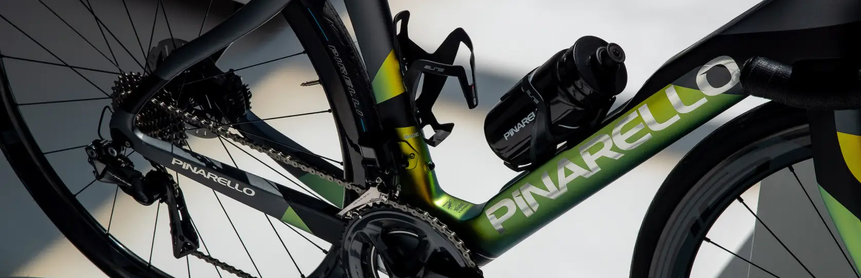 Rear-triangle detail of the Pinarello × Hani Dogma F12 summer colorway, iridescent green-gold paint across the chainstay and seat tube with Pinarello bottle cages and the chrome Pinarello wordmark reading across the down tube