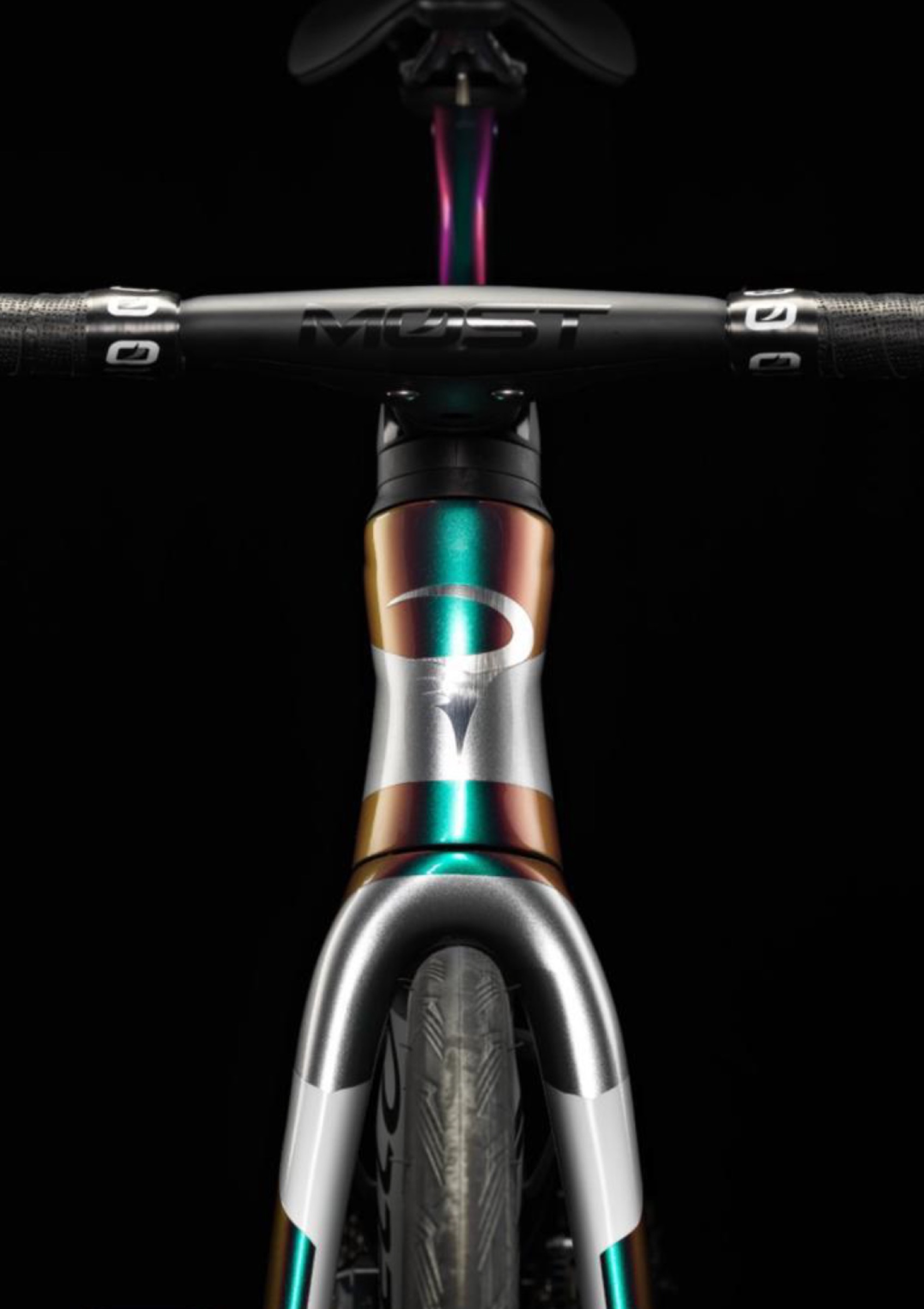 Head-on view of the Dogma F12 head tube and fork crown — iridescent teal, copper, and silver paint shifting across the Pinarello logo, MOST handlebars above, carbon fork below