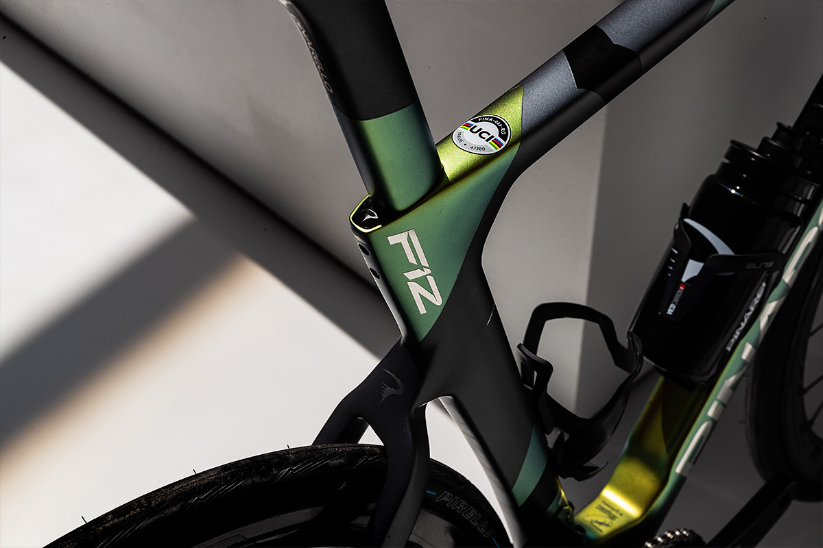 Detail of the Dogma F12 seat tube cluster showing F12 branding, UCI approval sticker, and iridescent green-gold paint finish