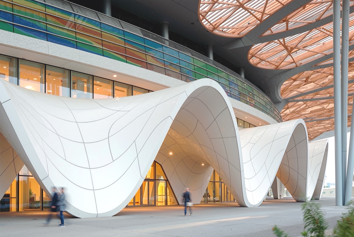 Ground-level view of the undulating white facade panels with flowing curvilinear seams as pedestrians pass beneath a timber lattice canopy roof with circular skylights