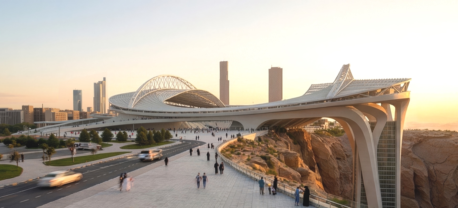 Street-level panoramic view of the arena elevated above the cliff with pedestrians on a landscaped promenade at sunset