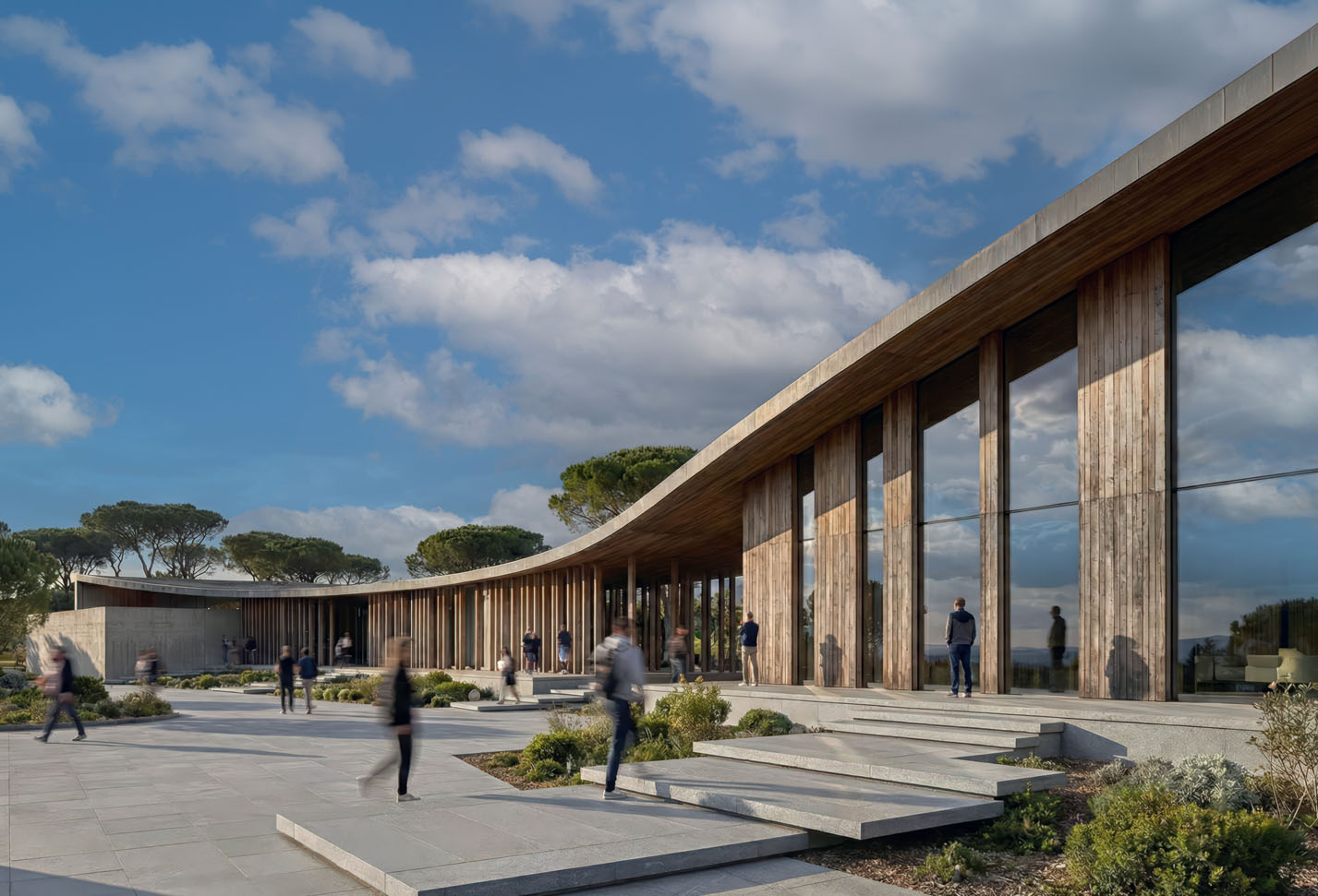Curved timber wave pavilion with colonnade and landscaped public plaza beneath Mediterranean pines