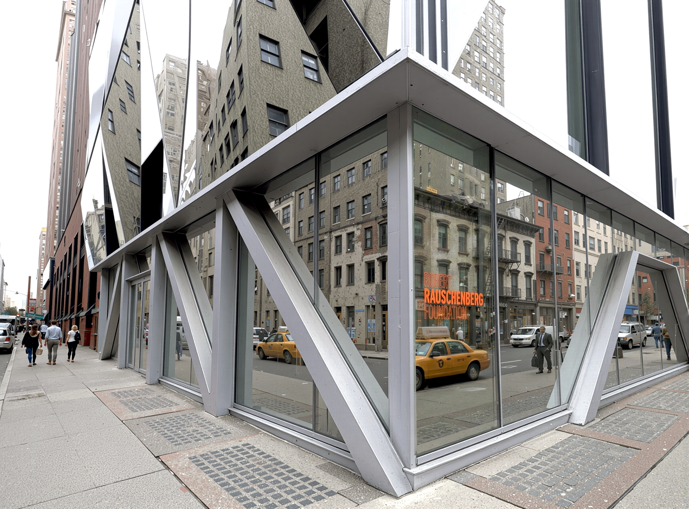 Ground-level detail of the corner entrance with angular steel structural members framing large glass panels and the Rauschenberg Foundation signage