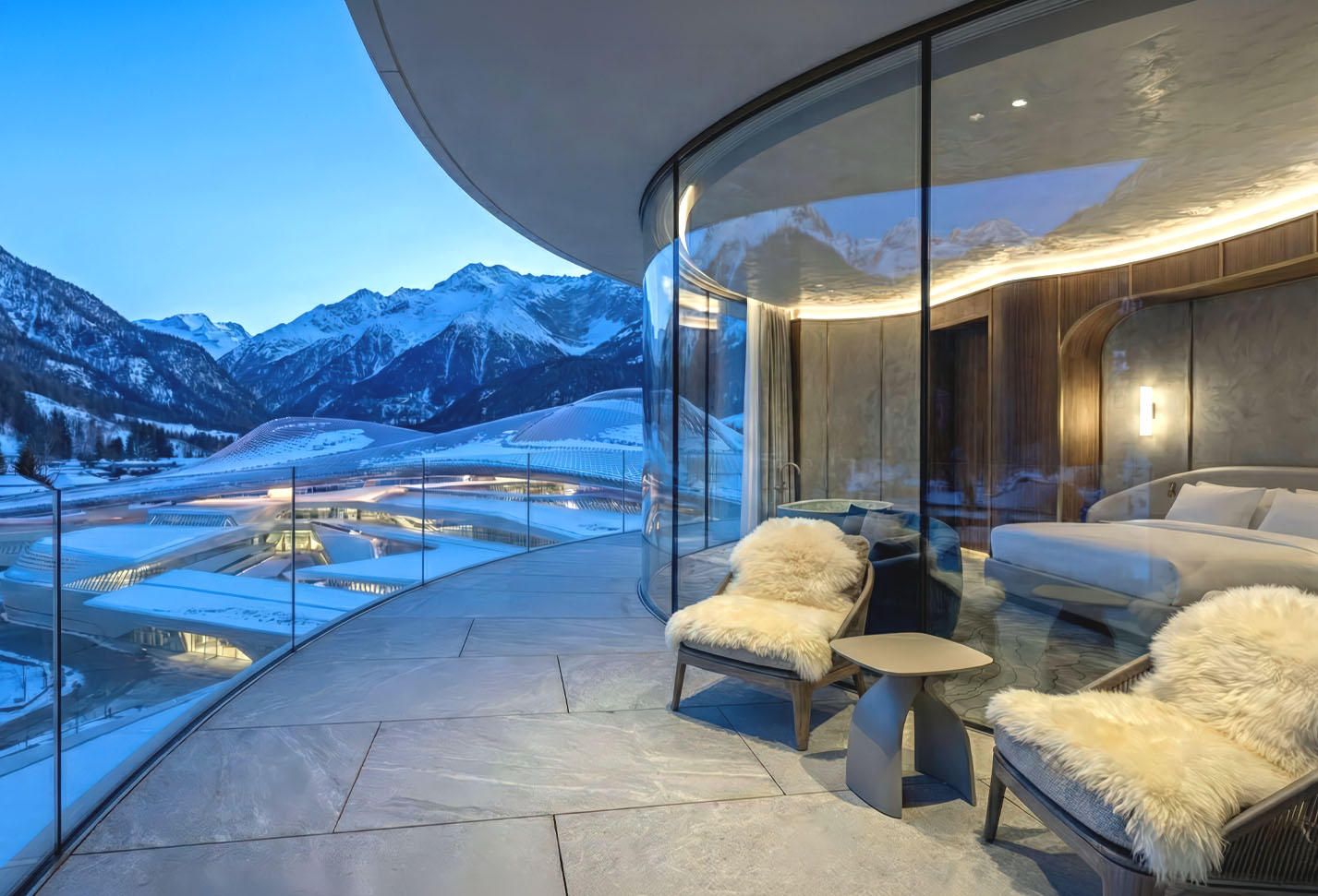 Curved glass terrace suite with panoramic Dolomite mountain views and sheepskin lounge seating