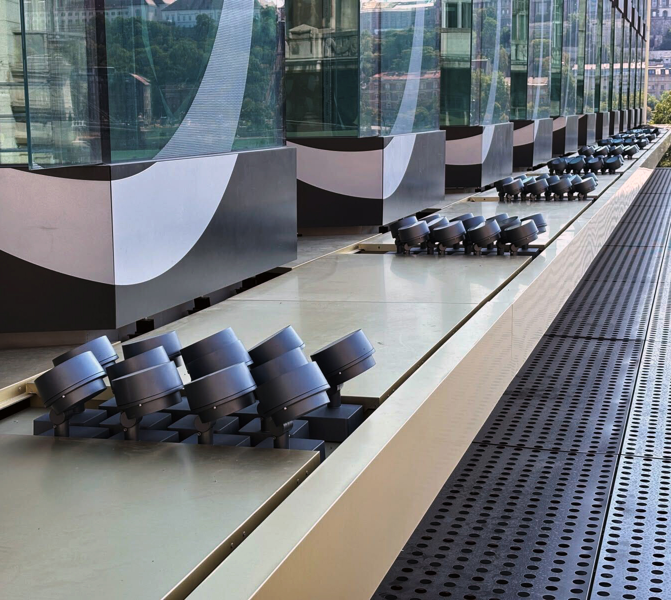 Parapet-level view along the SO/ Budapest facade, the row of exterior spot-light fixtures aimed up at the Op Art glass panels, Buda reflected in the surface