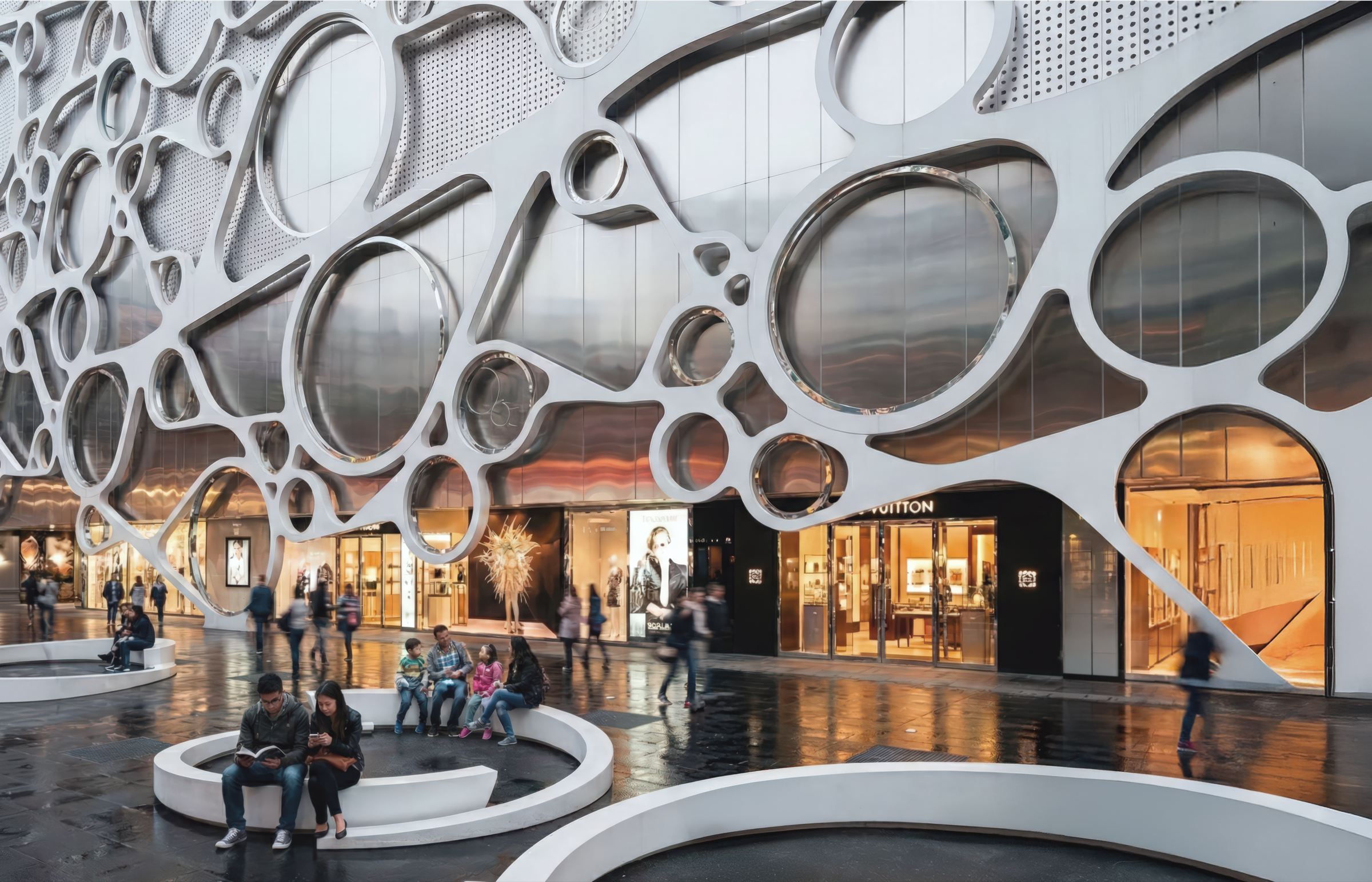 Street-level exterior view of the organic white lattice facade with circular and elliptical openings of varying scale, visitors seated on a circular bench, and the illuminated Louis Vuitton storefront visible through the structural openings