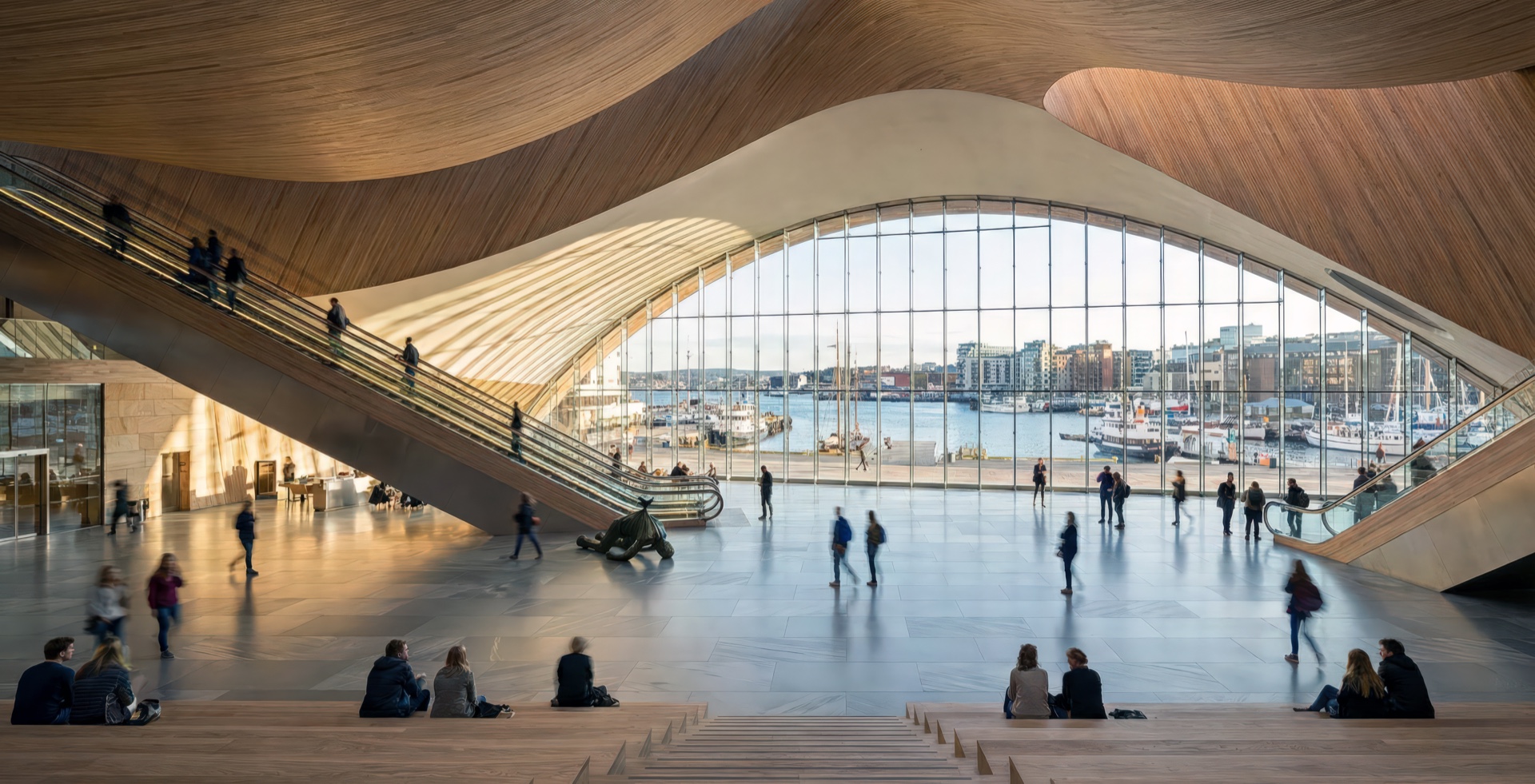 Grand atrium hall with sweeping sculptural timber ceiling canopy, monumental arched window framing the Oslo waterfront, cascading escalators, and broad timber seating steps filled with visitors