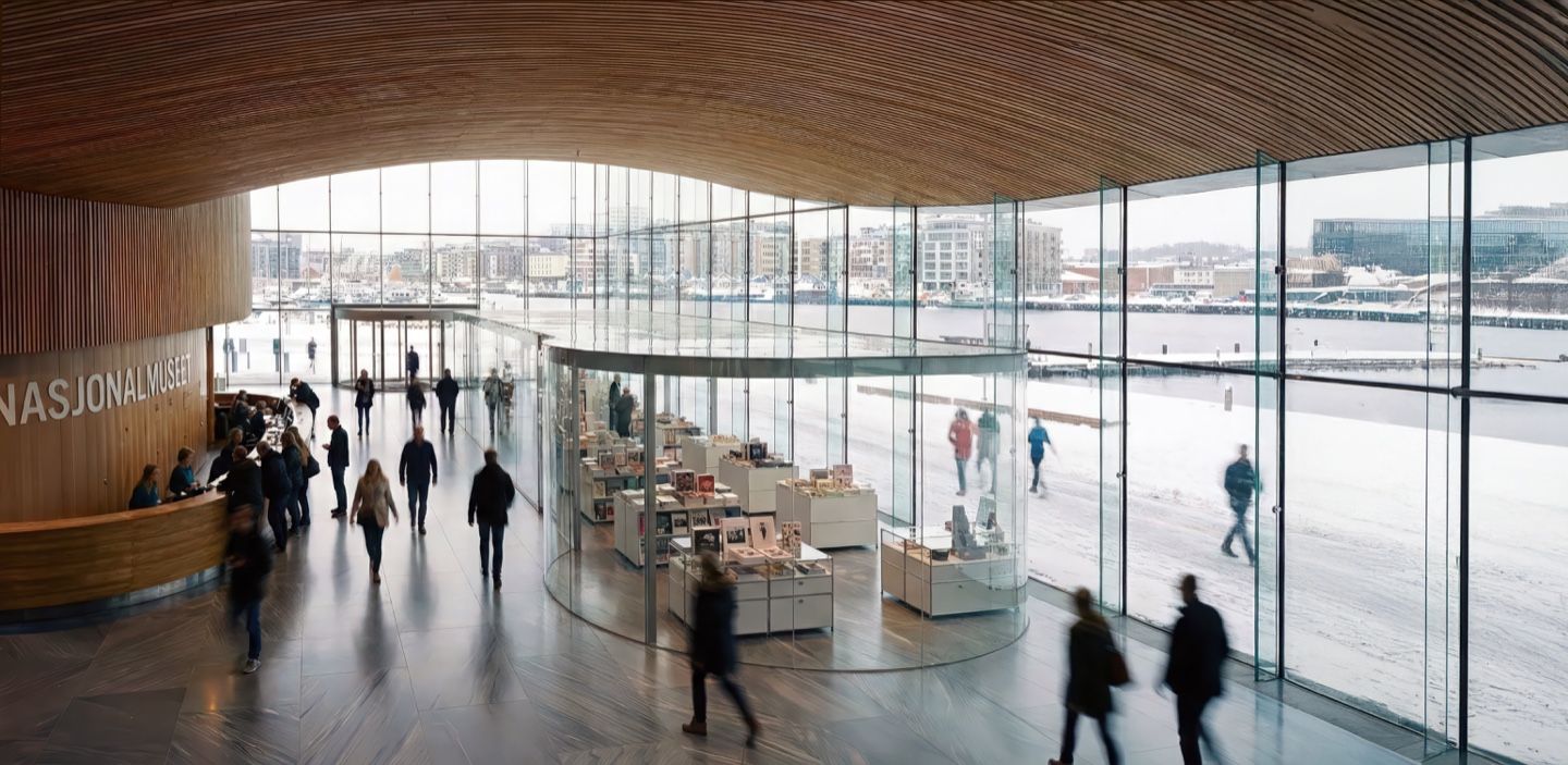 Wide view of the museum lobby showing the timber reception desk, glass gift shop volume, and full-height glazed facade with views across the waterfront to the city