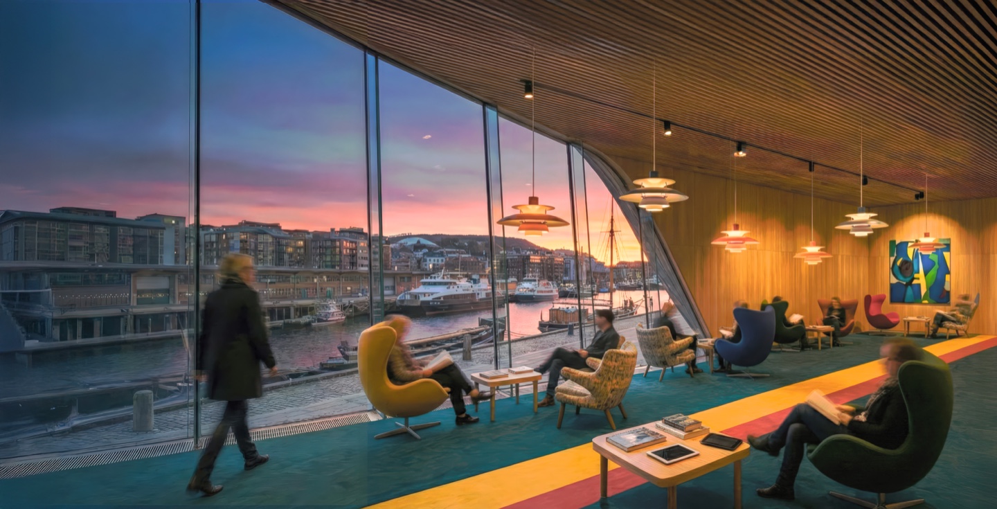 Wide angle of the reading room showing a visitor walking past colorful lounge seating, dramatic sunset light through the curved glass facade, and pendant lights suspended from the slatted timber ceiling
