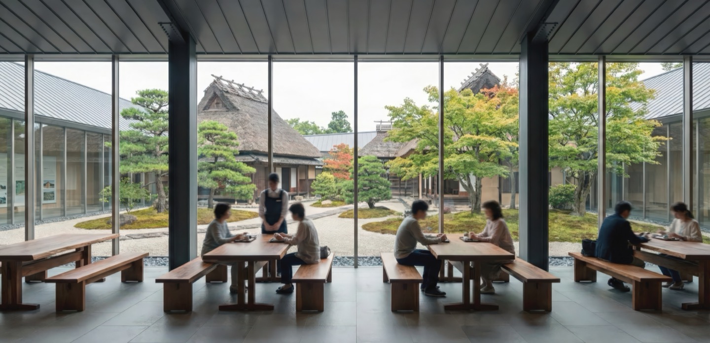 Interior communal seating area with wooden benches and floor-to-ceiling glass framing a traditional Japanese farmhouse and autumn garden