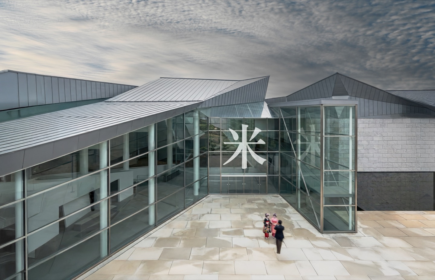 Tohoku Agrarian Museum entrance courtyard with angular metallic rooflines and floor-to-ceiling glass facades displaying the kanji character for rice