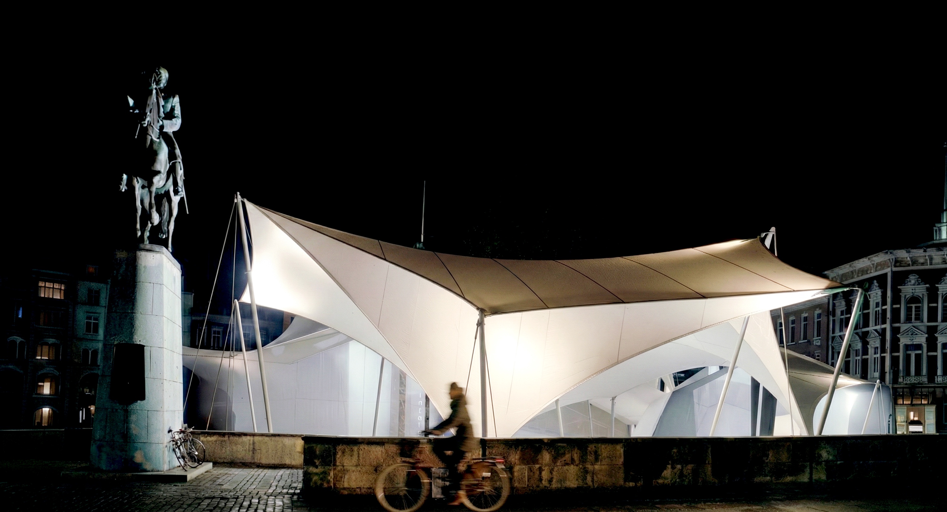 Panoramic night view of the Univers Theater illuminated tensile structure with historic statue in Bispetorv Square, Aarhus