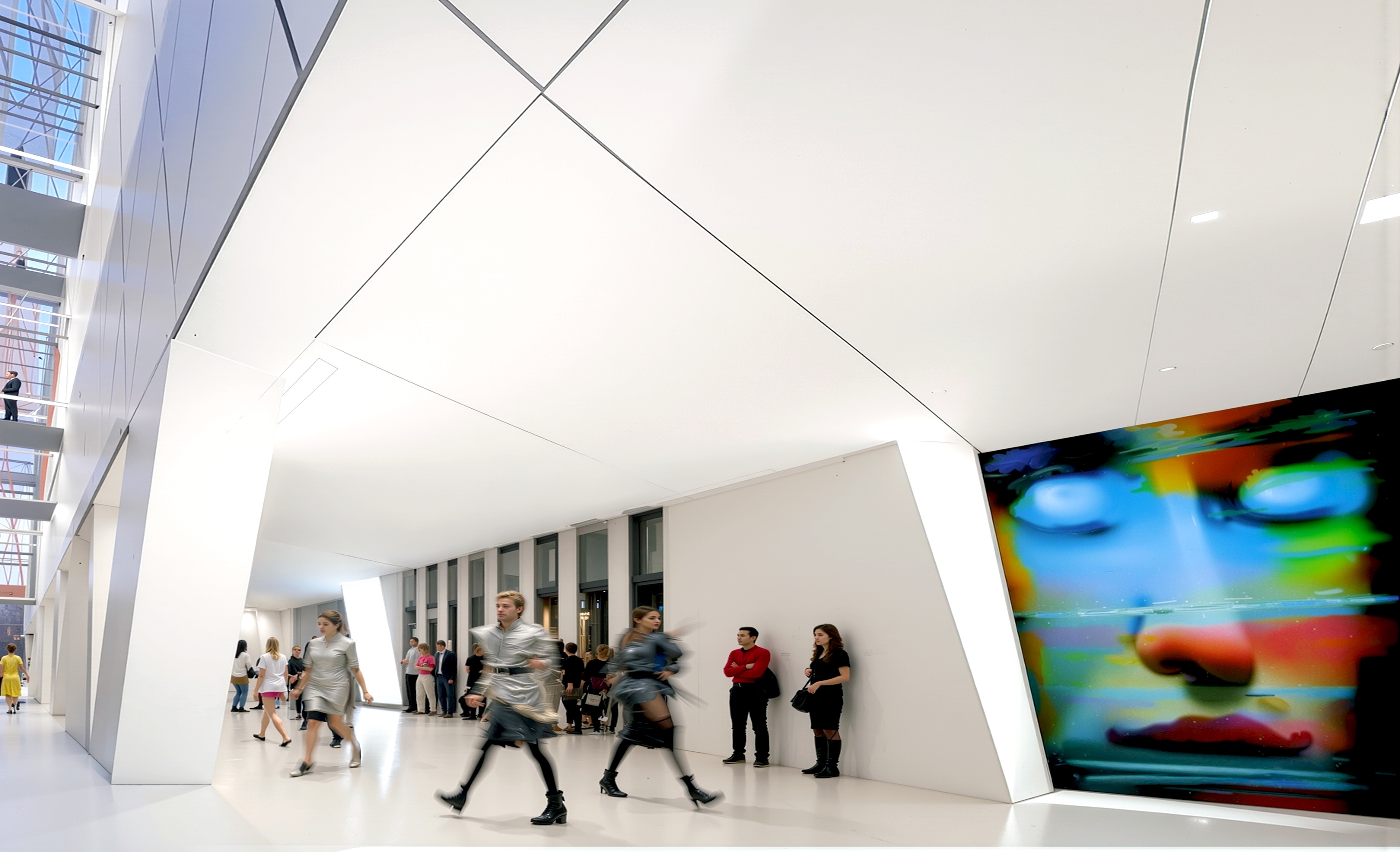 Interior atrium with angular white walls, visitors, and a large-scale digital art display