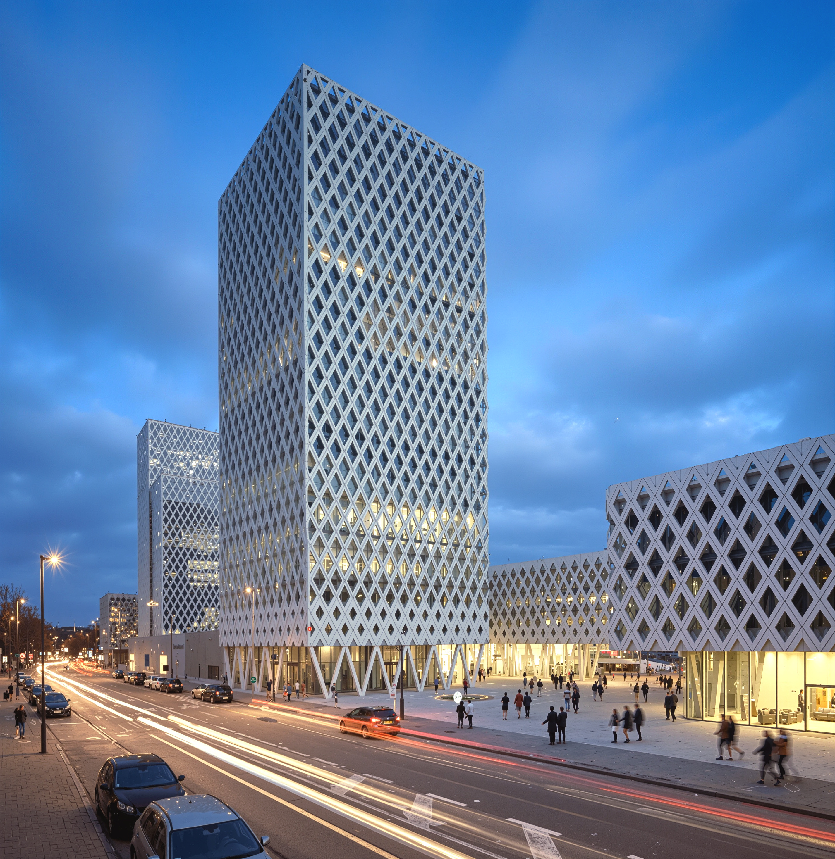 Illuminated main tower at night with diamond-lattice facade and car light trails on the street