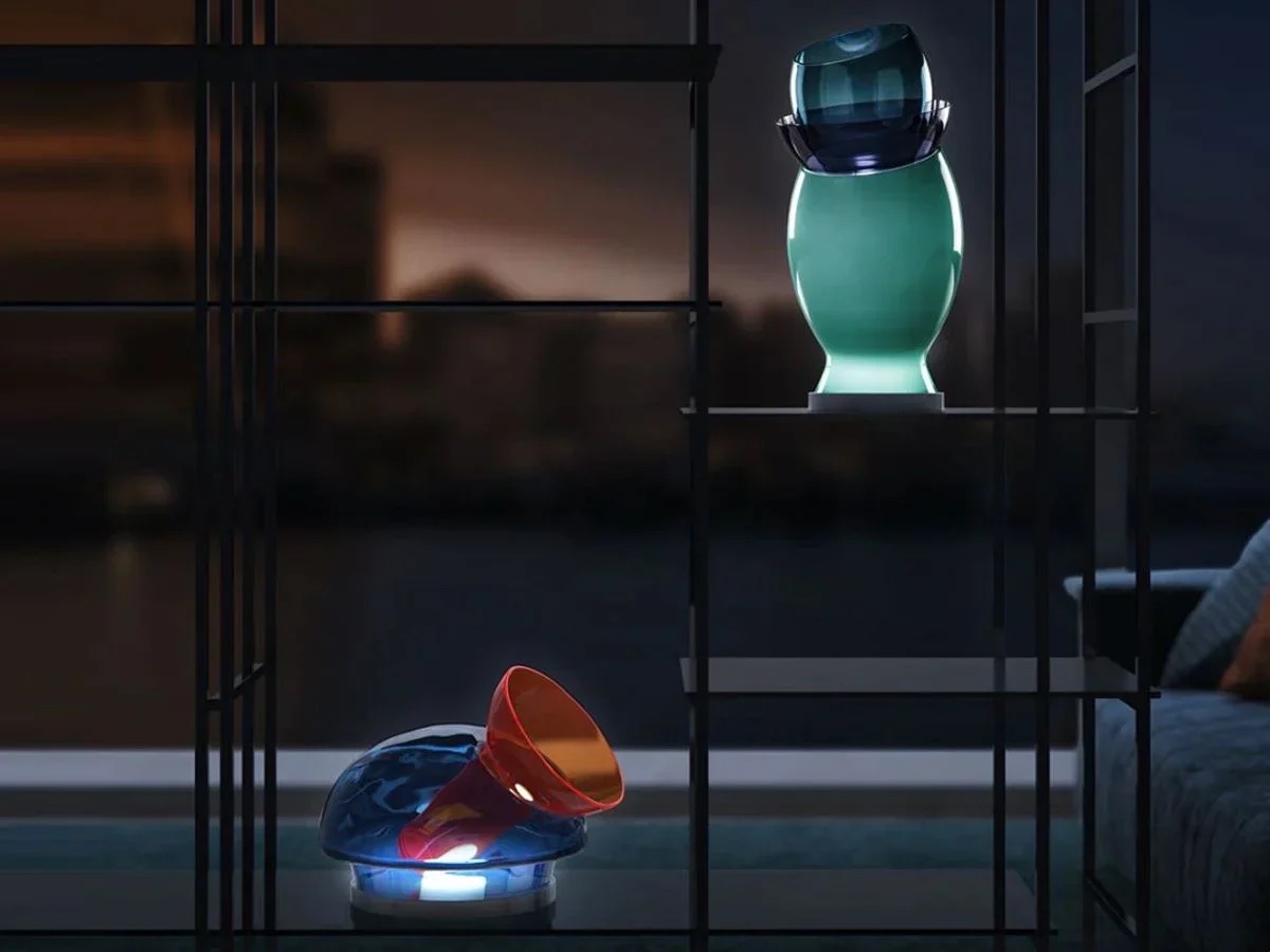 Two illuminated Luminosita glass light sculptures by Asymptote for Venini displayed on glass shelving against a twilight window