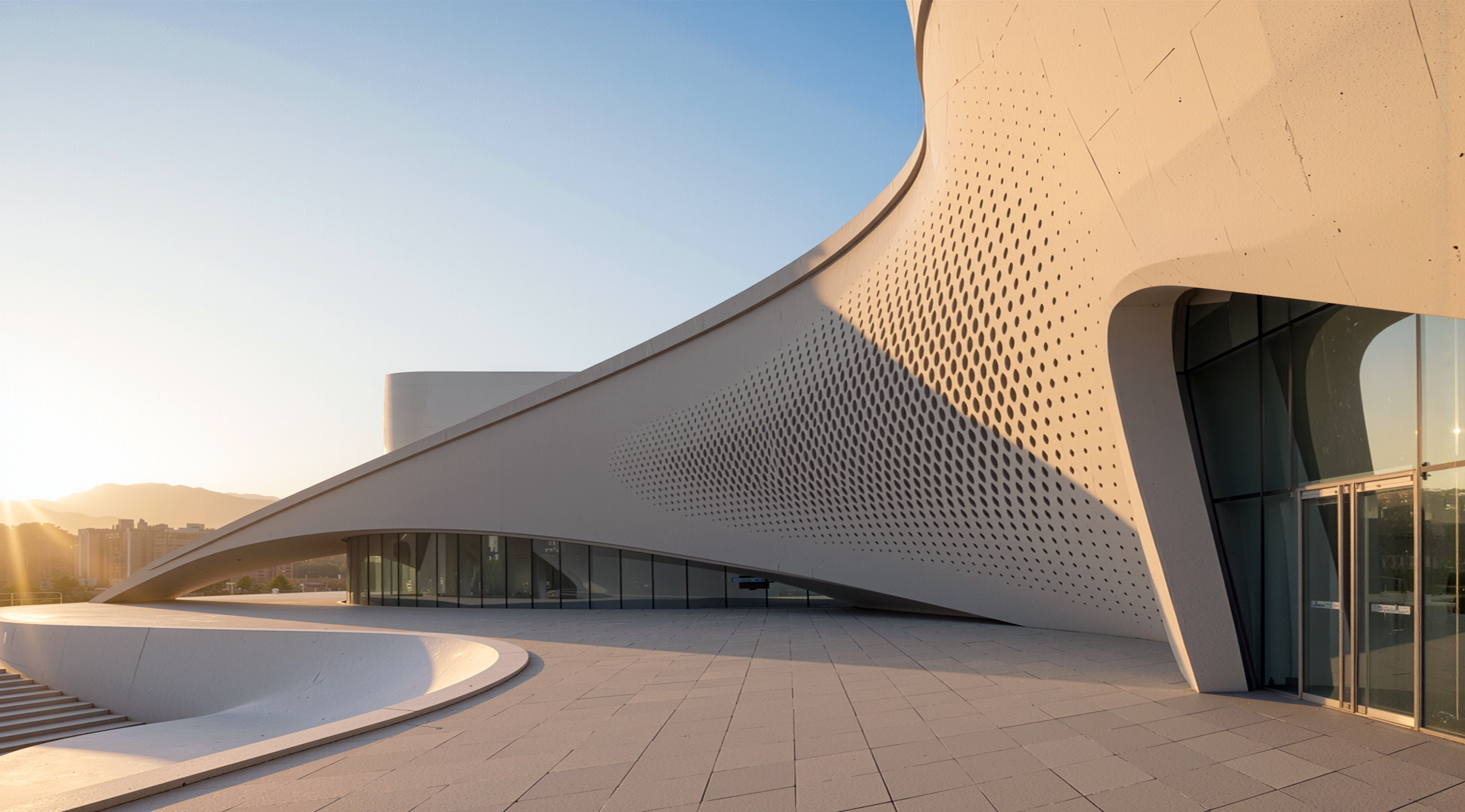 Close-up of the perforated concrete facade at golden hour with shadows cast through circular openings and sweeping curves above the glazed ground floor