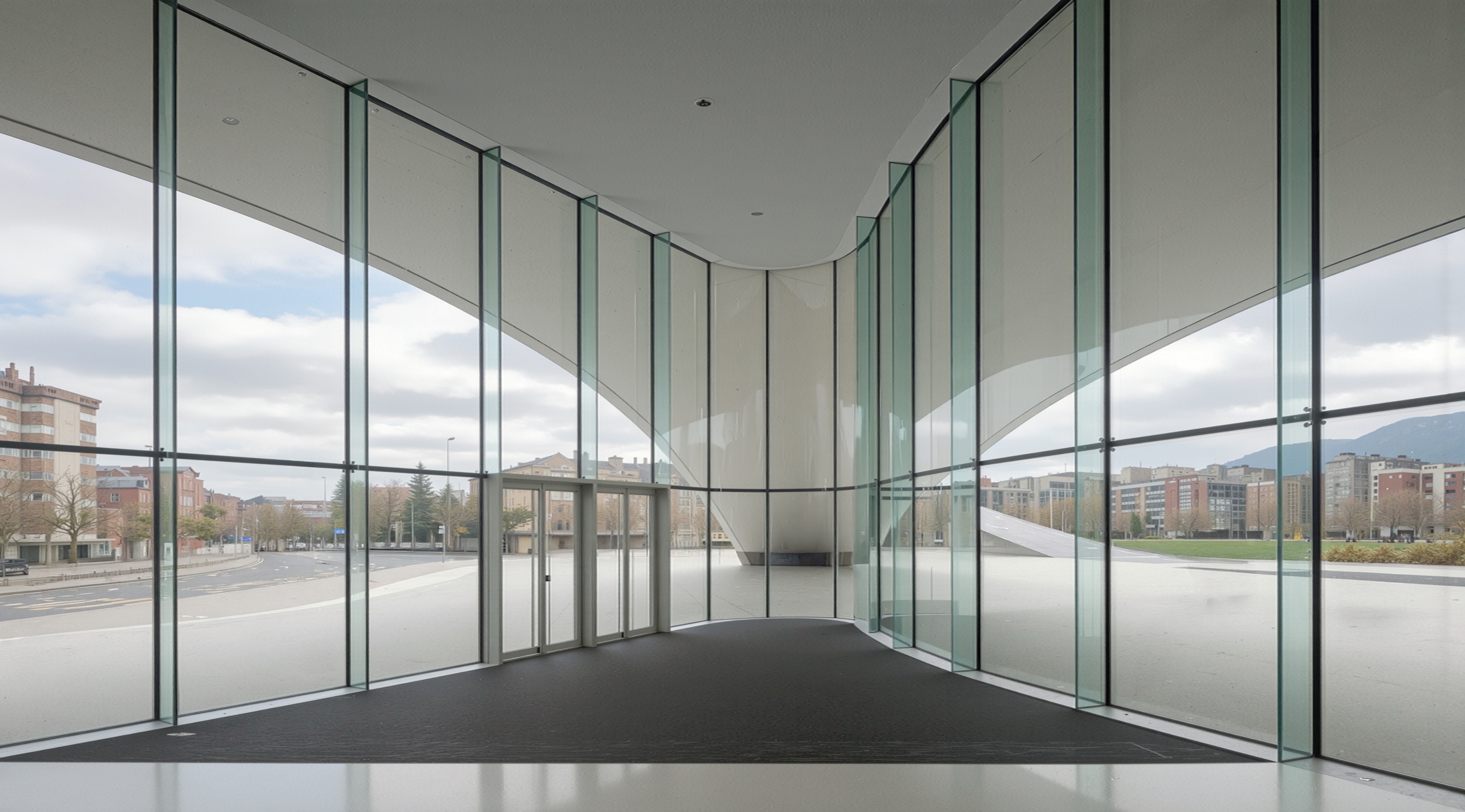 Ground-floor glass-walled corridor offering panoramic views of the surrounding plaza and city through floor-to-ceiling curved glazing