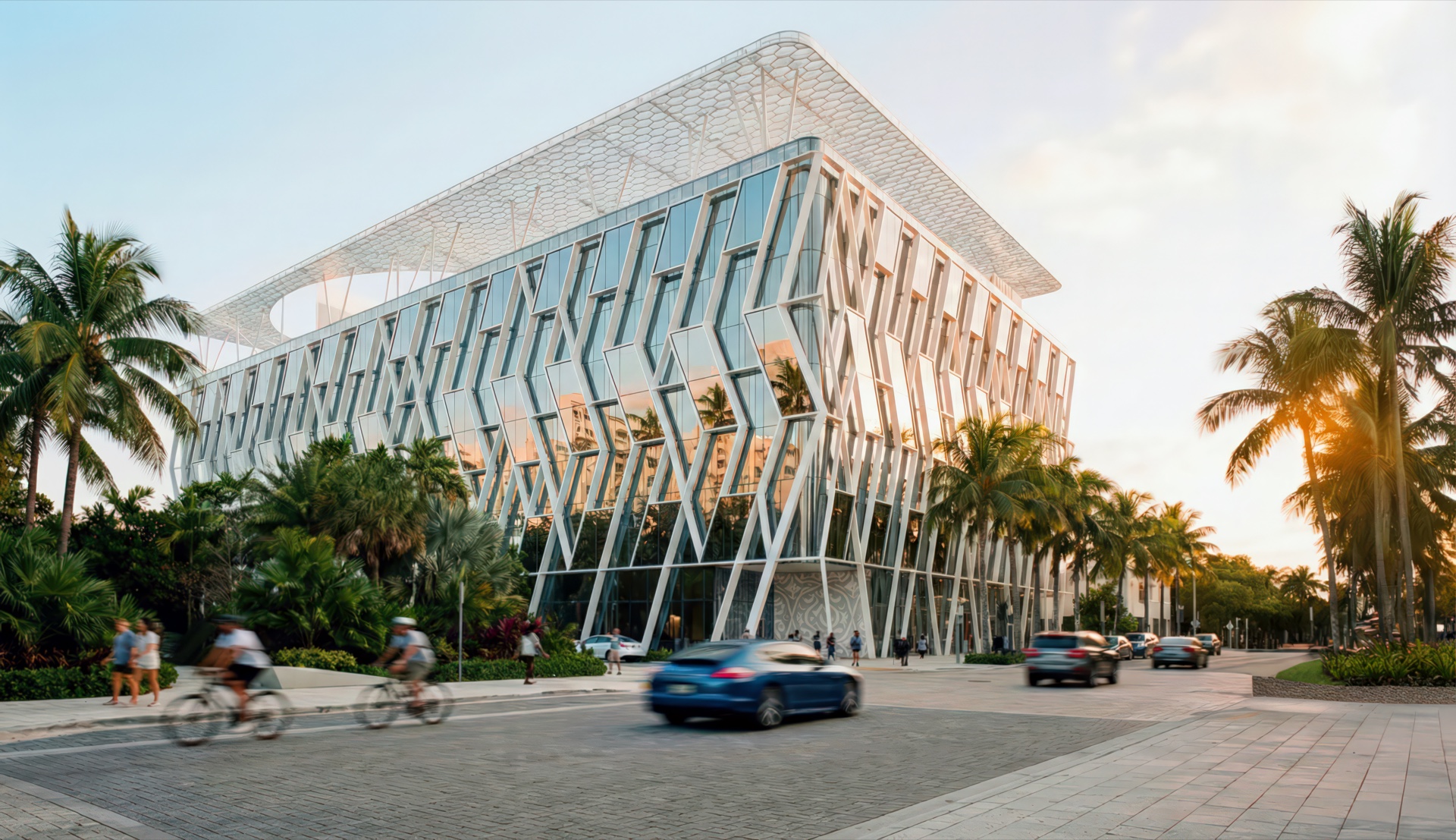 Wide street-level view of the Vogel Fitness Complex set among tropical landscaping and palm trees with cyclists and cars passing at dusk