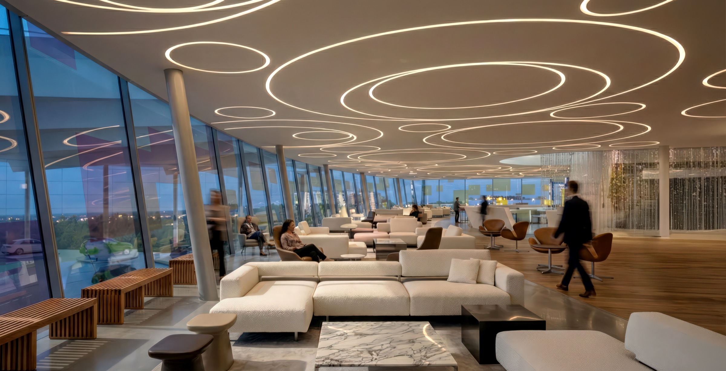 Sky lounge at dusk with the ring-patterned ceiling glowing warmly, guests seated in conversation areas, twilight visible through the continuous glazing, and a crystal curtain partition at right