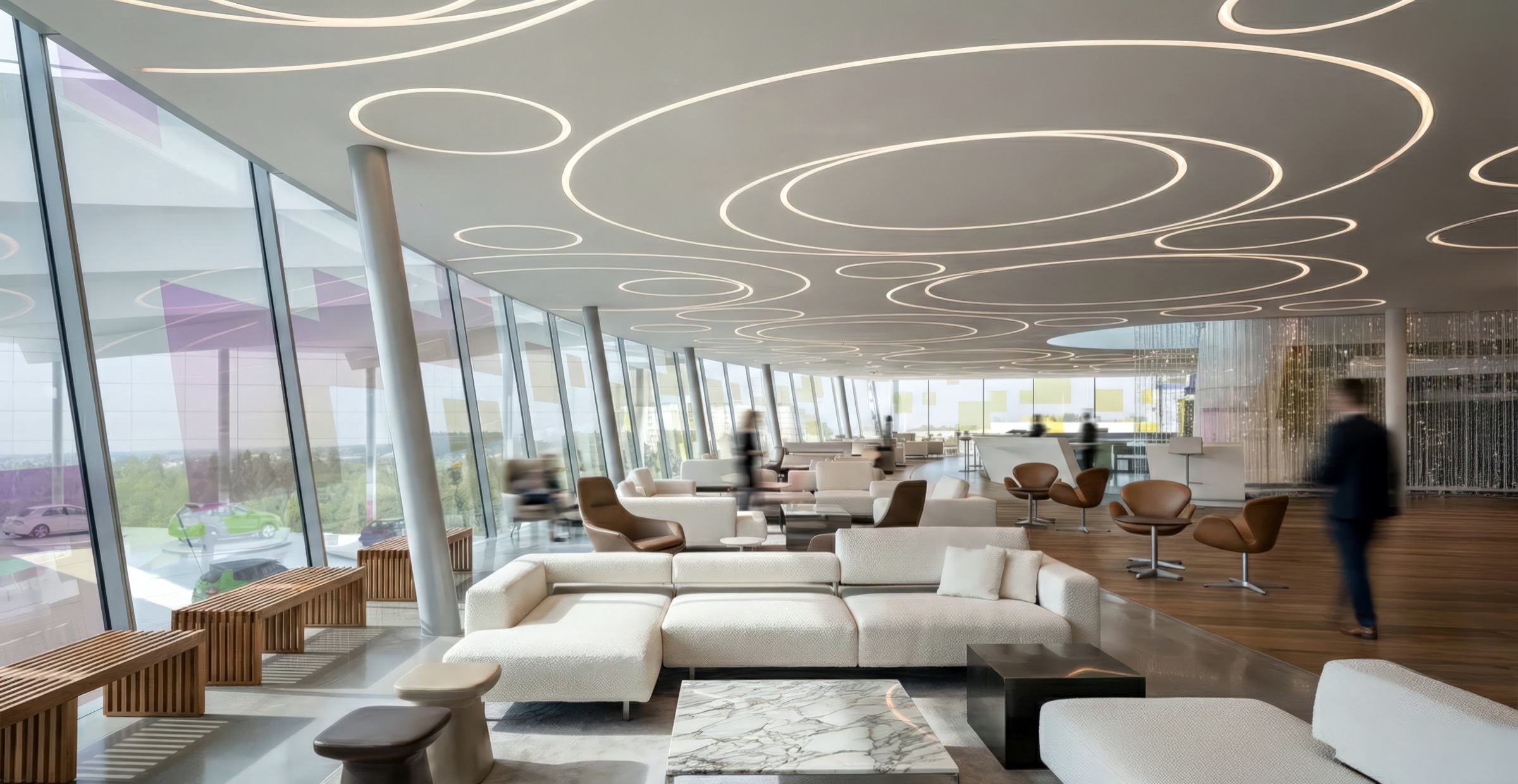 Expansive upper-level sky lounge with organic ring-patterned LED ceiling, panoramic floor-to-ceiling glazing, white sectional sofas, marble coffee tables, leather Swan chairs, and timber benches along the glass wall