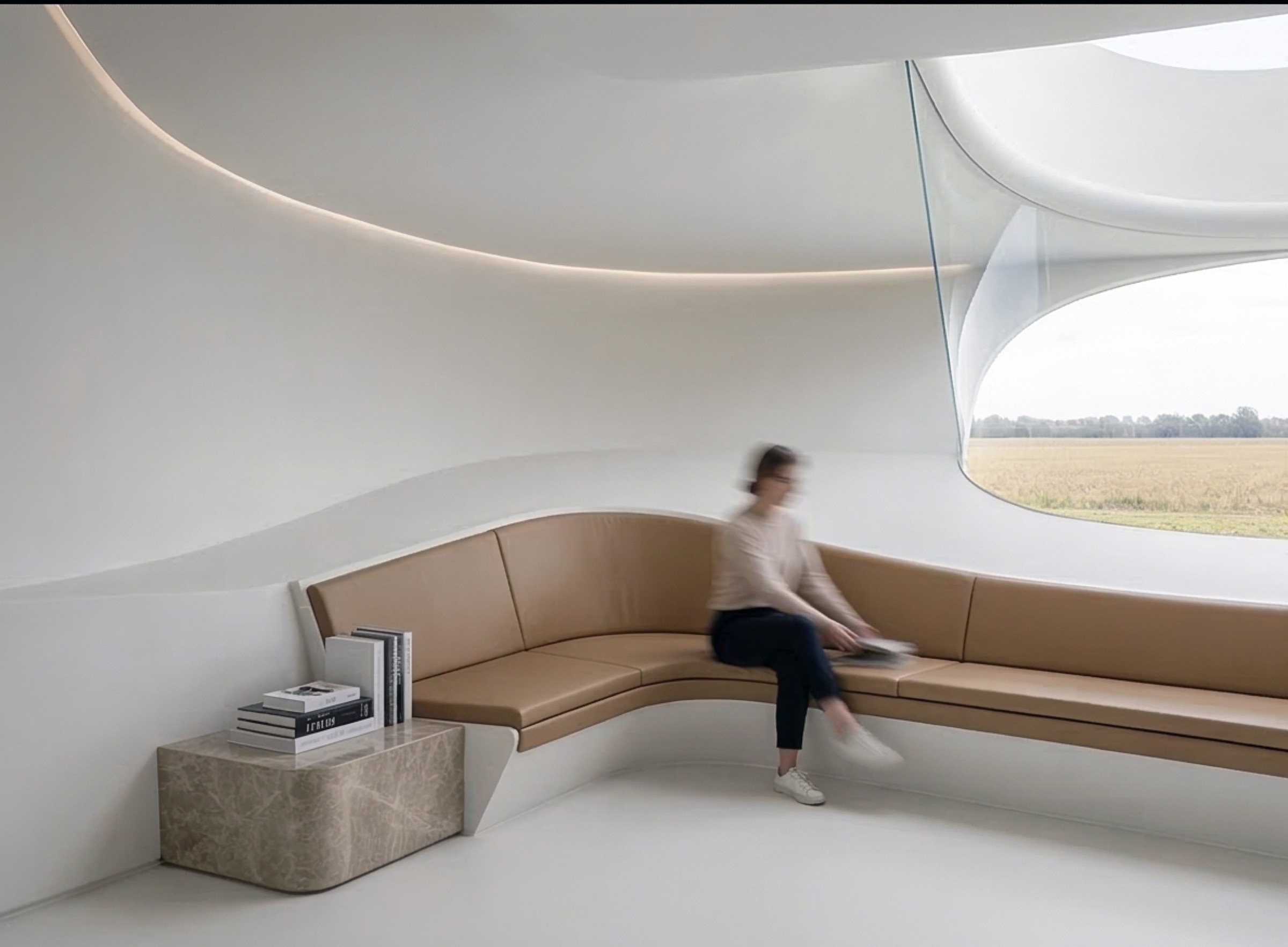 A curved leather banquette built into the white shell wall beside a large organic-shaped window looking out over golden summer fields, with books stacked on a marble side table
