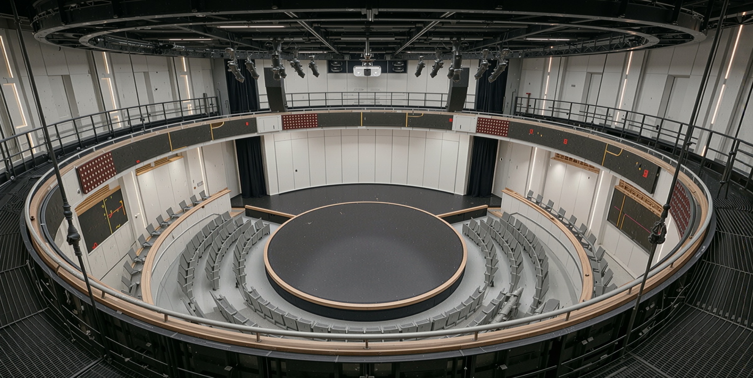 Panoramic view of the circular theater-in-the-round auditorium from above, showing the rotating black stage disc, surrounding tiered seating, technical rigging galleries, and the cylindrical volume of the hall