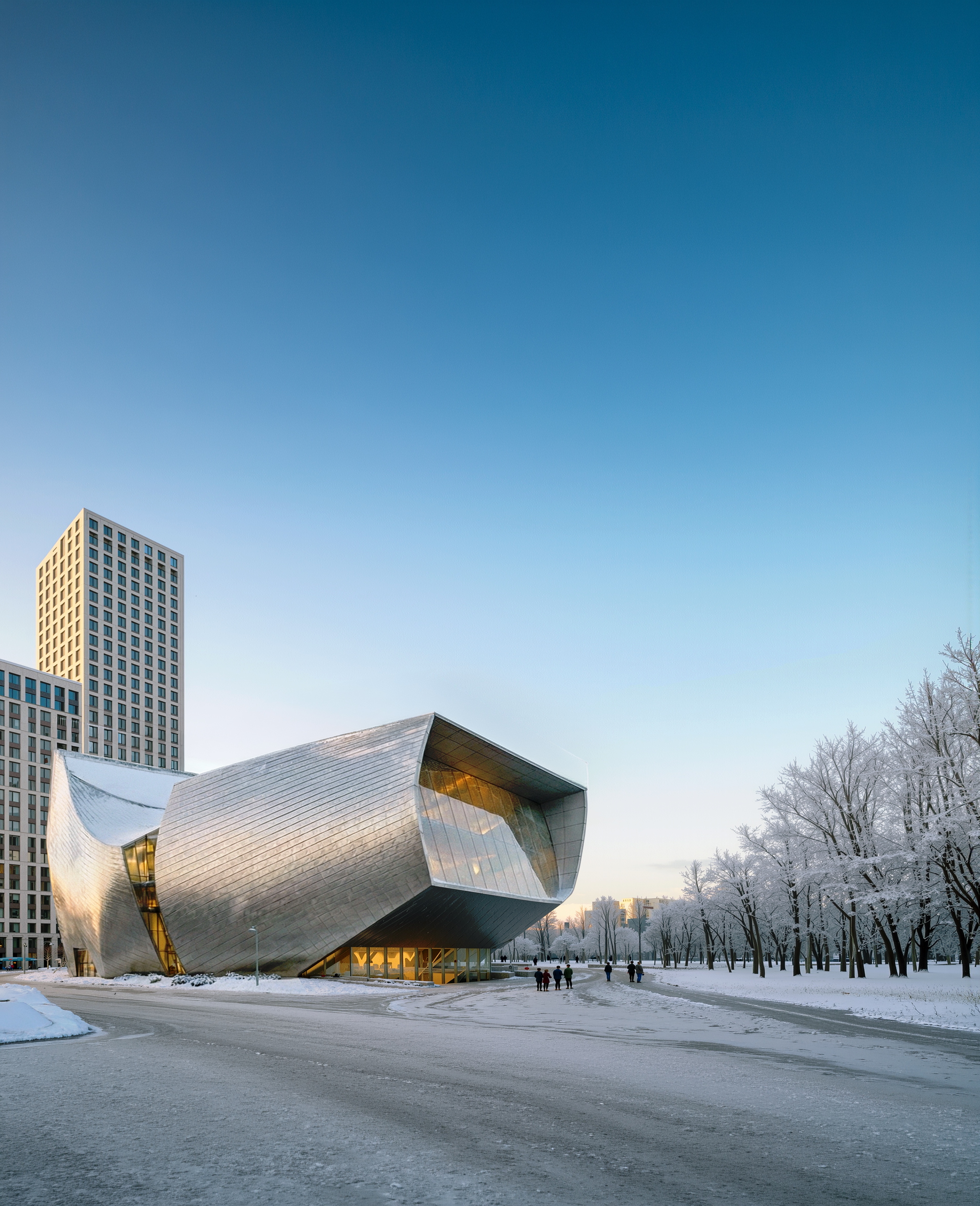 Winter portrait view of the ZIL Performing Arts Center with its metallic facade reflecting sunlight against a clear blue sky and frost-covered trees